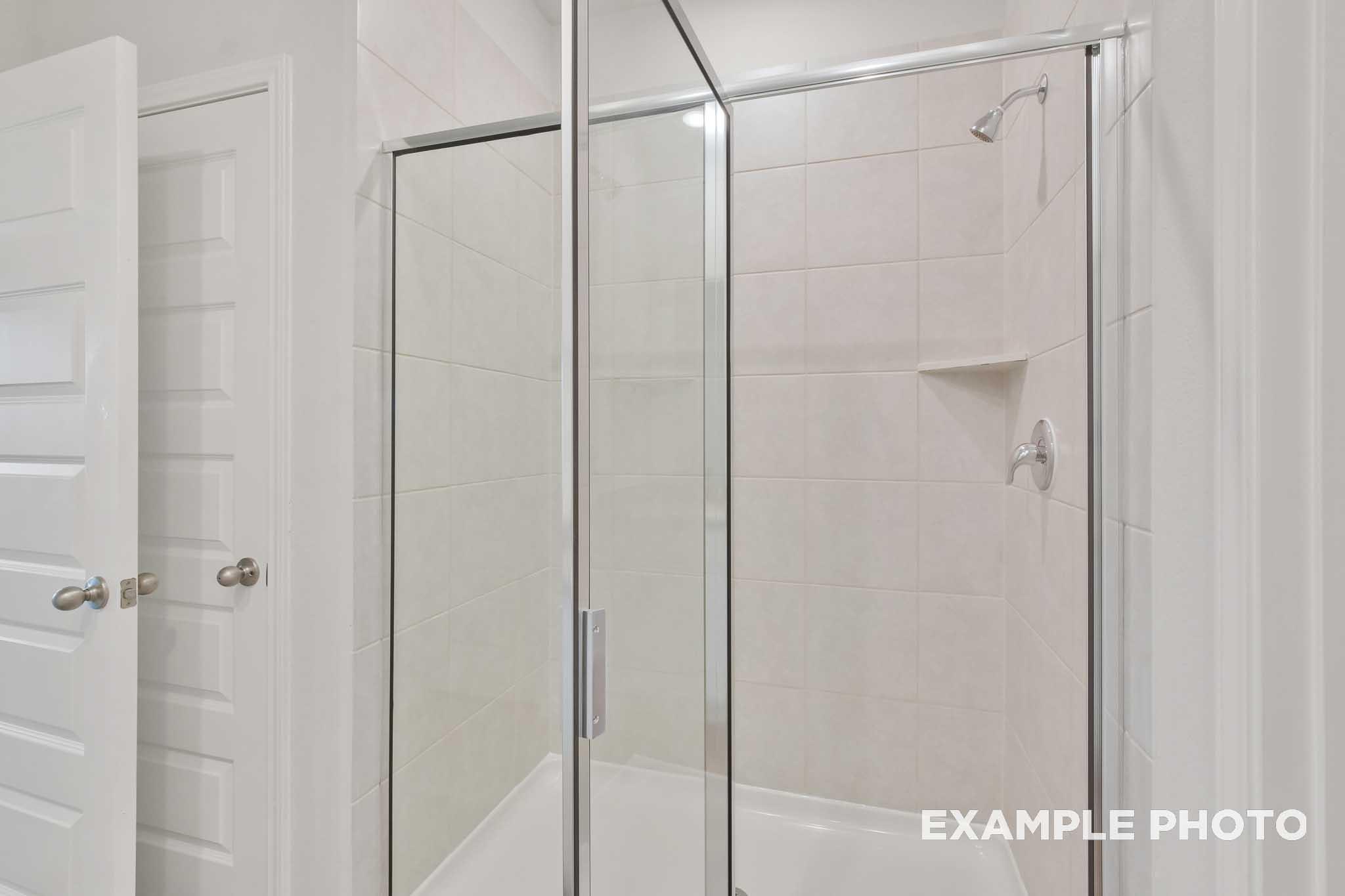 Glass-enclosed tile shower with brushed nickel fixtures in The Brazos master bathroom by Davidson Homes, Beasley, Texas