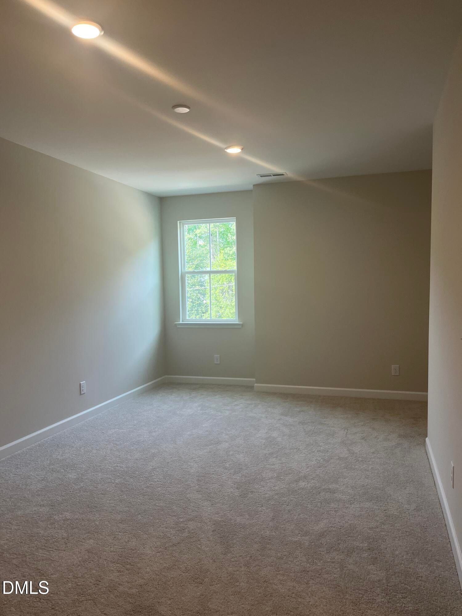 Bright empty bedroom with beige walls, gray carpet, large window, and recessed lights in Davidson Homes Ashport L, Wake Forest, NC