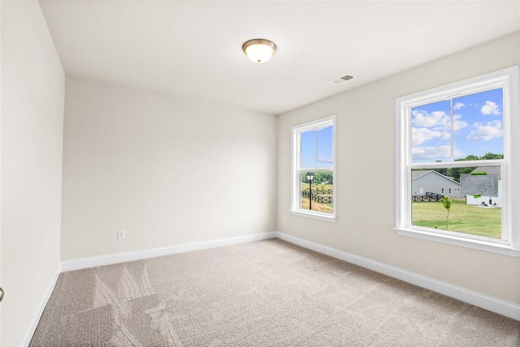 Bright secondary bedroom with window views of green fields and countryside in Davidson Homes The Hickory B at Wehunt Meadows, Hoschton, Georgia