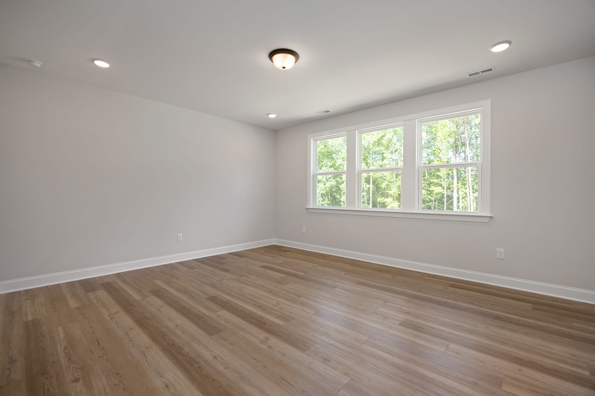 Spacious empty bedroom with light gray walls, oak hardwood floors, and large triple windows in Rockport, Wake Forest NC