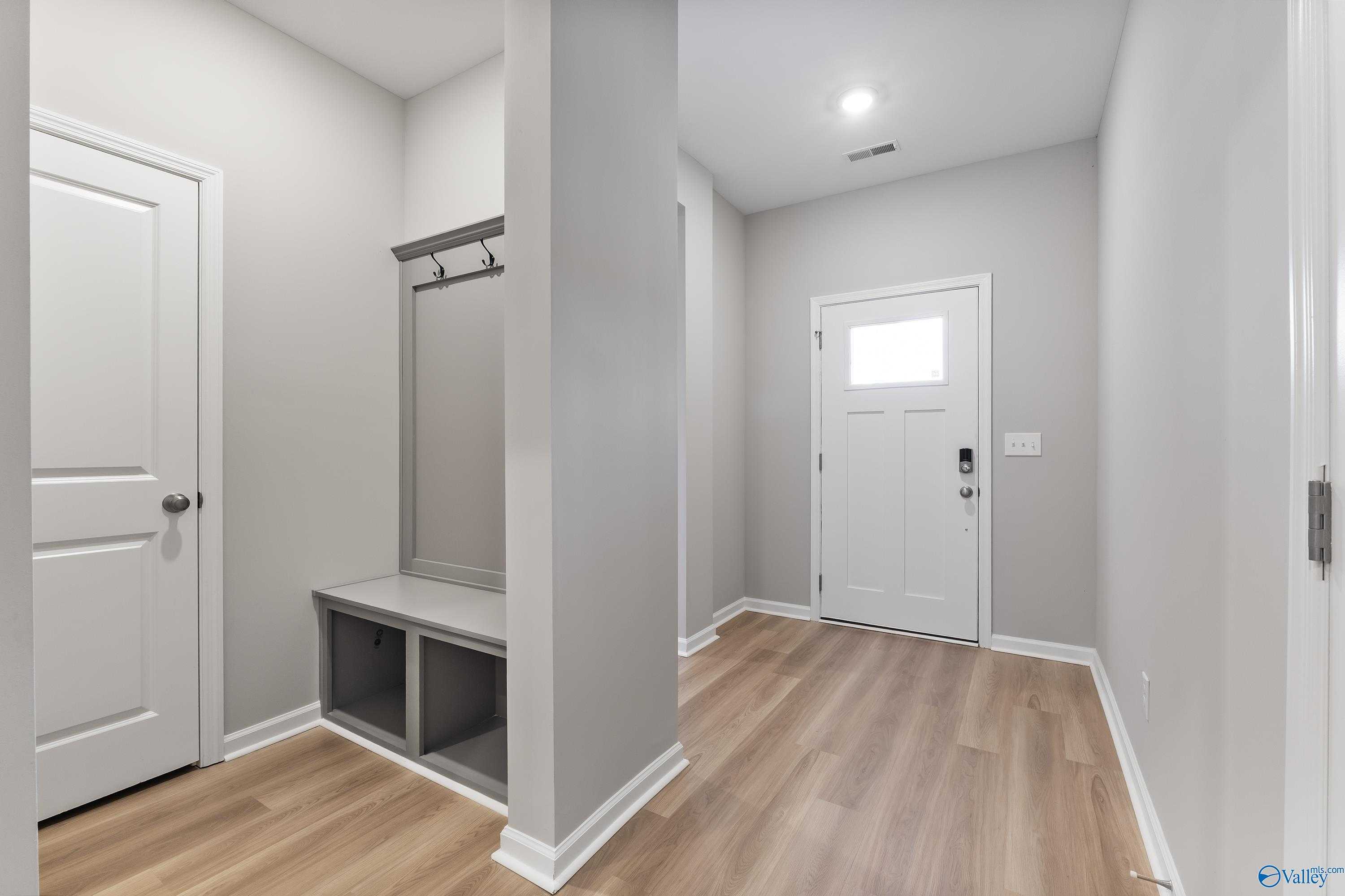 Modern entryway with built-in bench, coat hooks, light oak floors, and white doors in The Grace floor plan, Evergreen Mill, AL