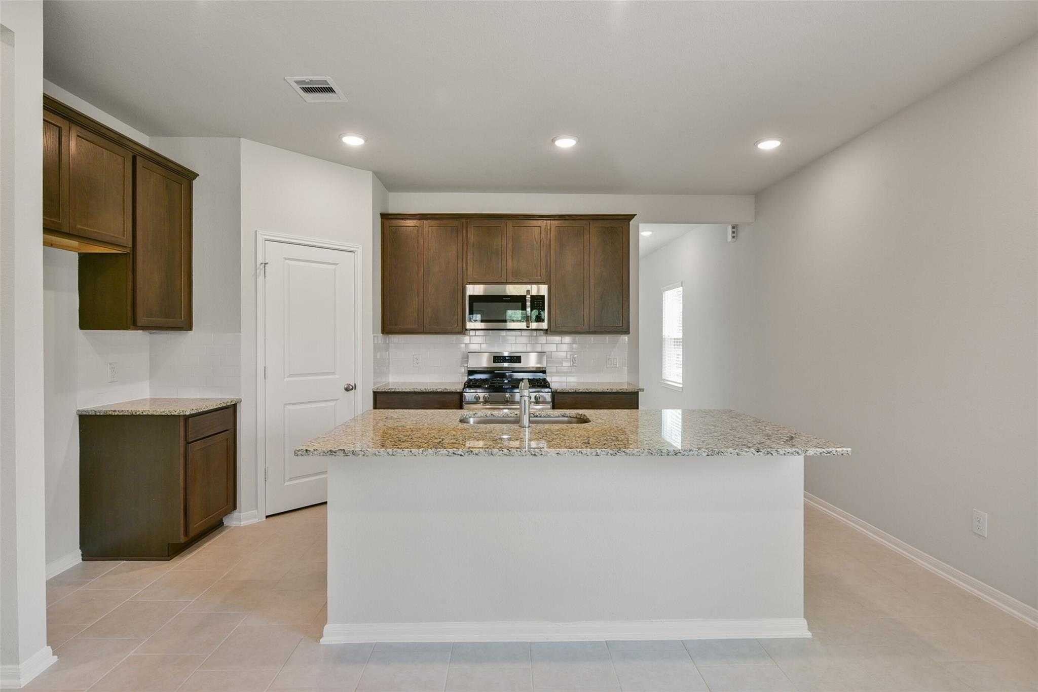 Modern kitchen featuring granite island, stainless steel appliances, and wood cabinets in The Sabine E floor plan, Dayton, TX