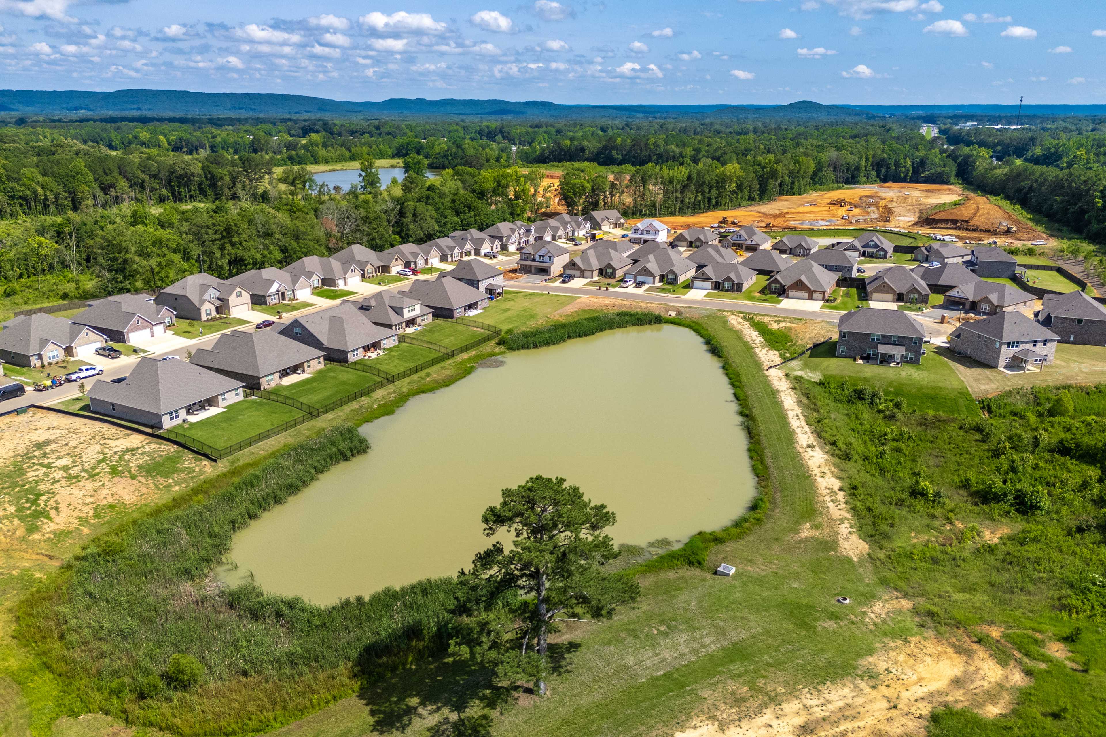 Aerial view of new gray-shingled homes curving around a serene pond in Cain Park, Hartselle Alabama by Davidson Homes