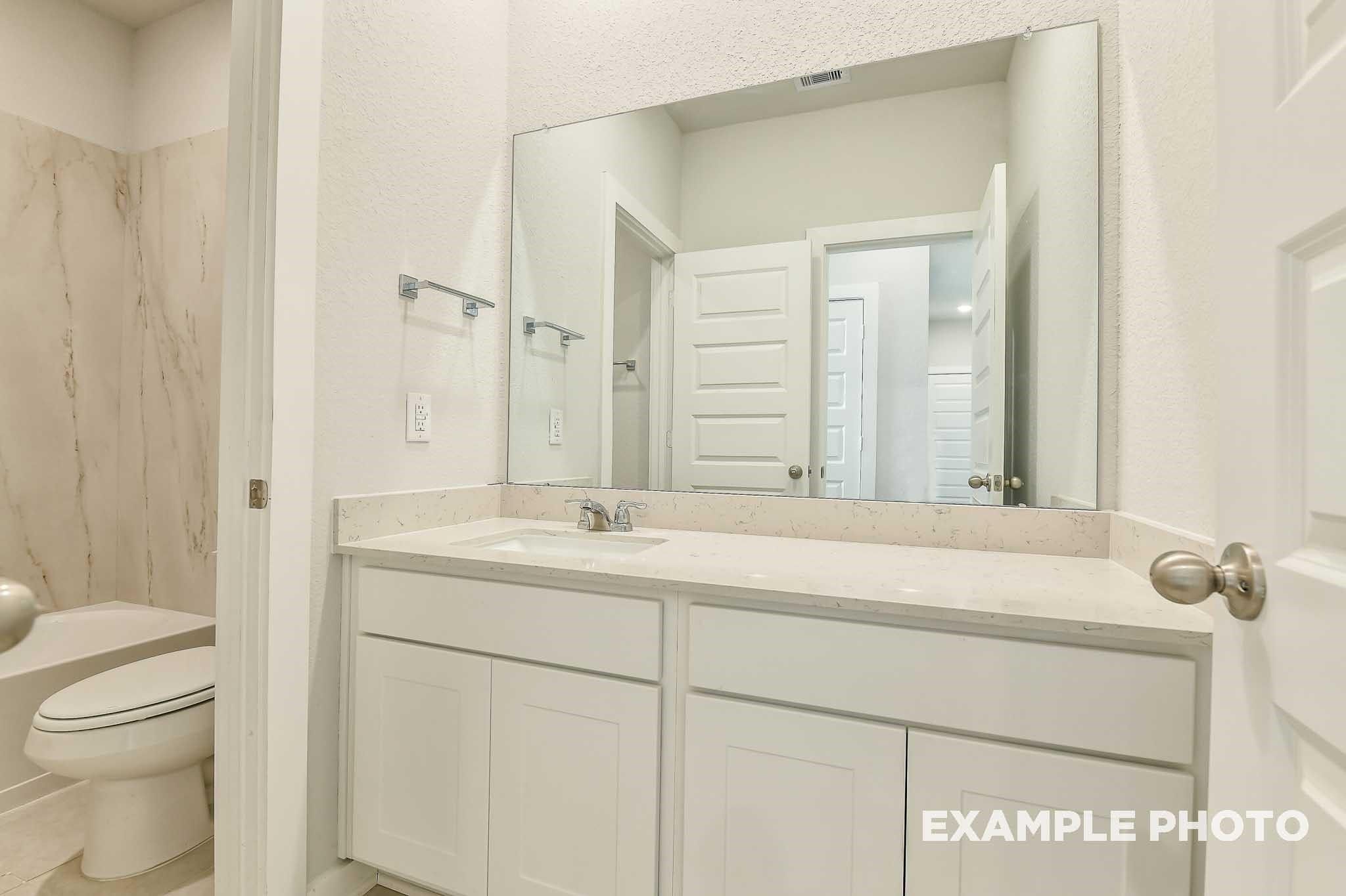 Modern master bathroom featuring double white vanity, large frameless mirror, and tiled shower in Davidson Homes The Colorado G, Conroe, Texas