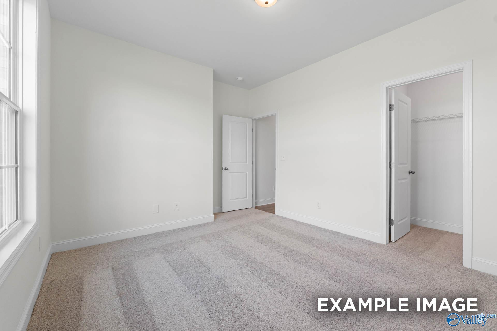 Bright secondary bedroom with white walls, neutral carpeting, open closet, and window in Davidson Homes The Rockford B, Athens AL