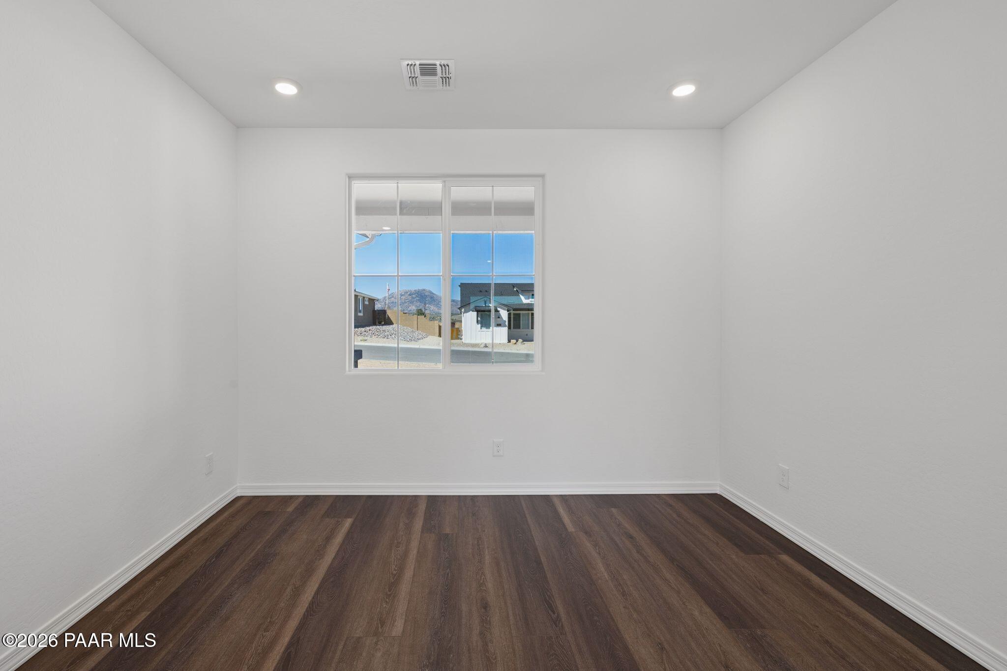 Bright empty room with hardwood floors, white walls, and large windows showcasing mountain views in The Monarch A, Prescott, Arizona