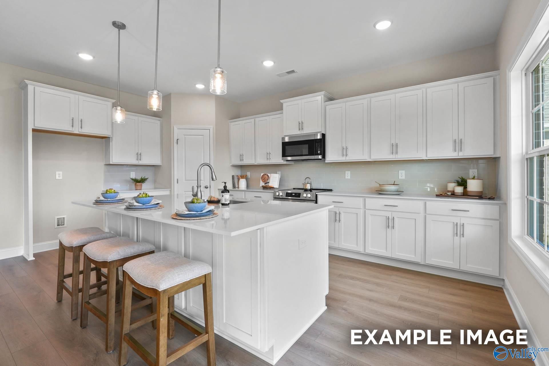 Modern white kitchen with large island, stainless appliances, pendant lights in Davidson Homes Madison A, Harvest, AL