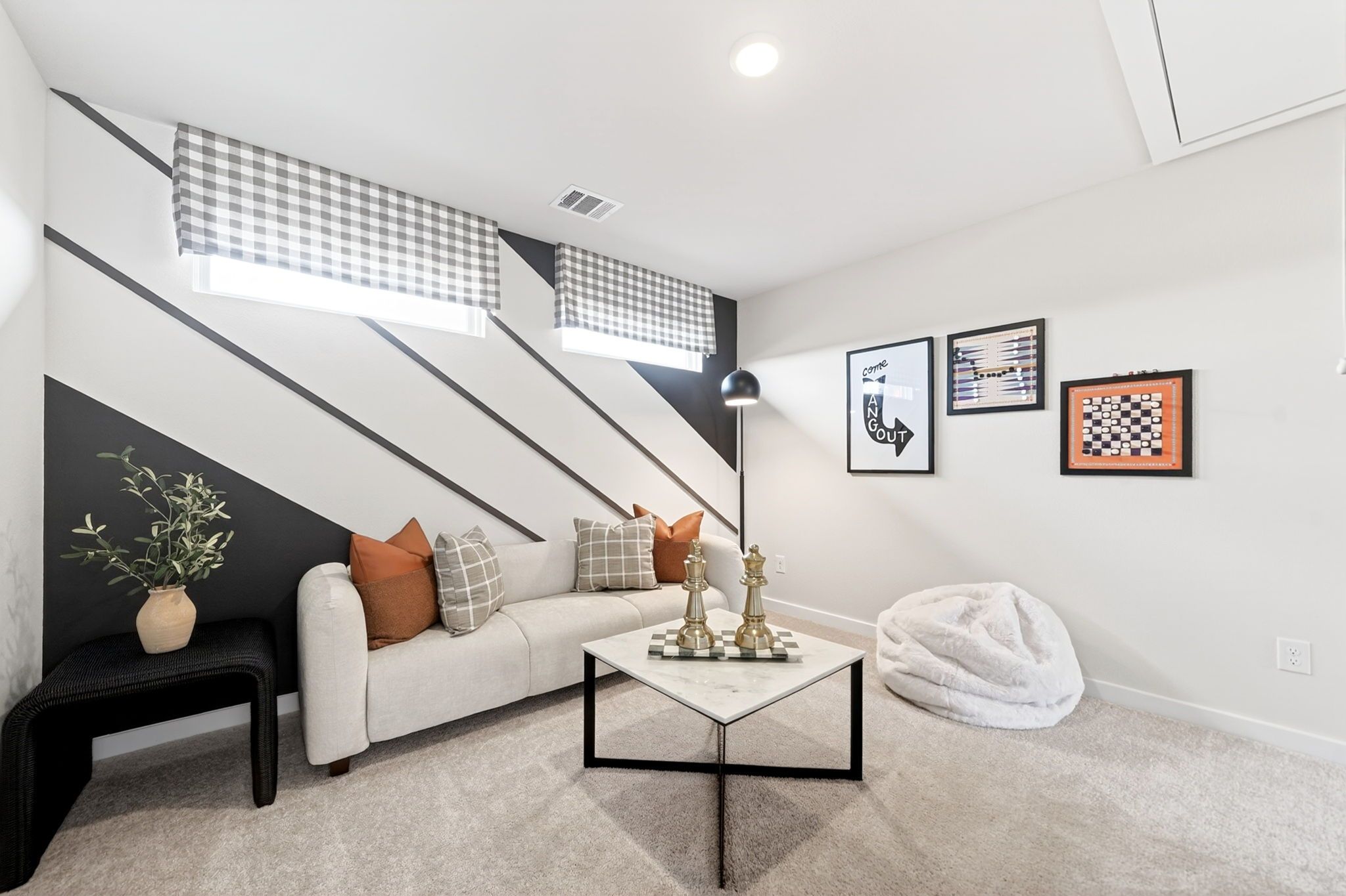 Cozy game room in Heartland Texas home with black-white striped walls, gingham curtains, beige sofa, marble chess table, and fluffy bean bag