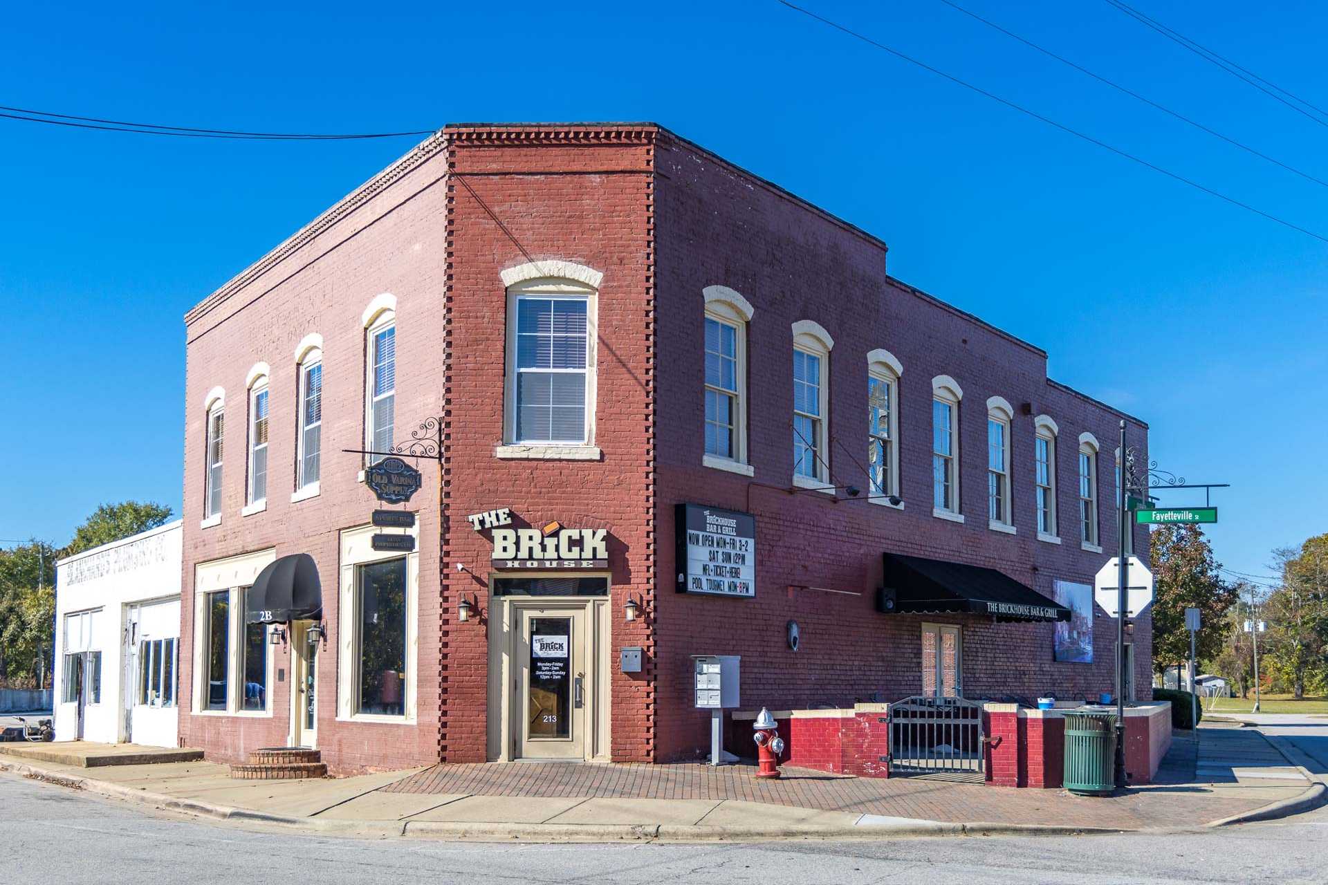 Red brick corner building with The Brick awning and signage in Fuquay-Varina NC near Prince Place community