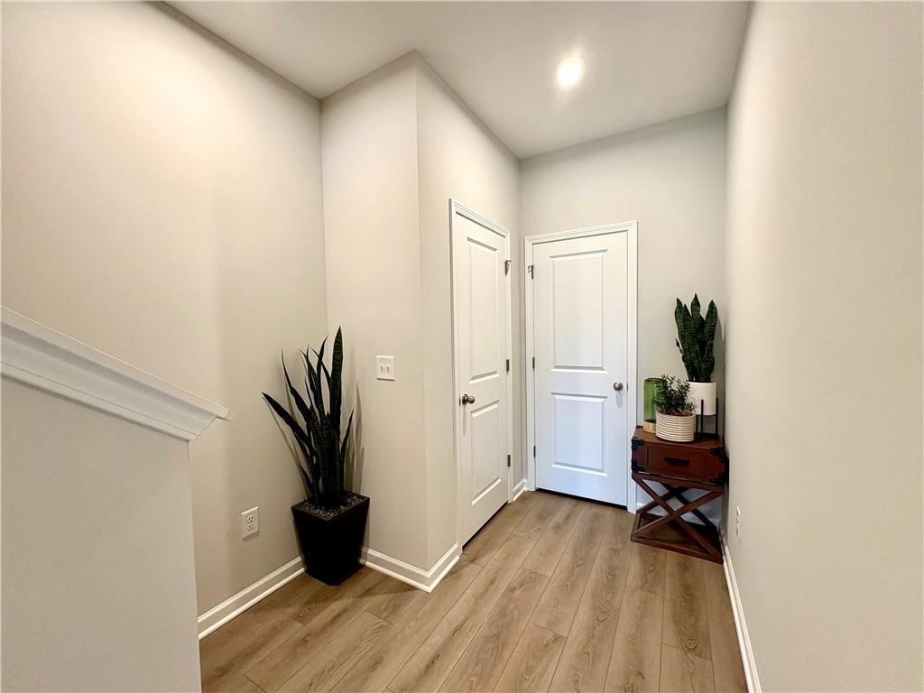 Bright entry hallway with beige walls, hardwood floors, staircase, louvered doors, and potted snake plants in The Monroe A by Davidson Homes, Emerson, GA