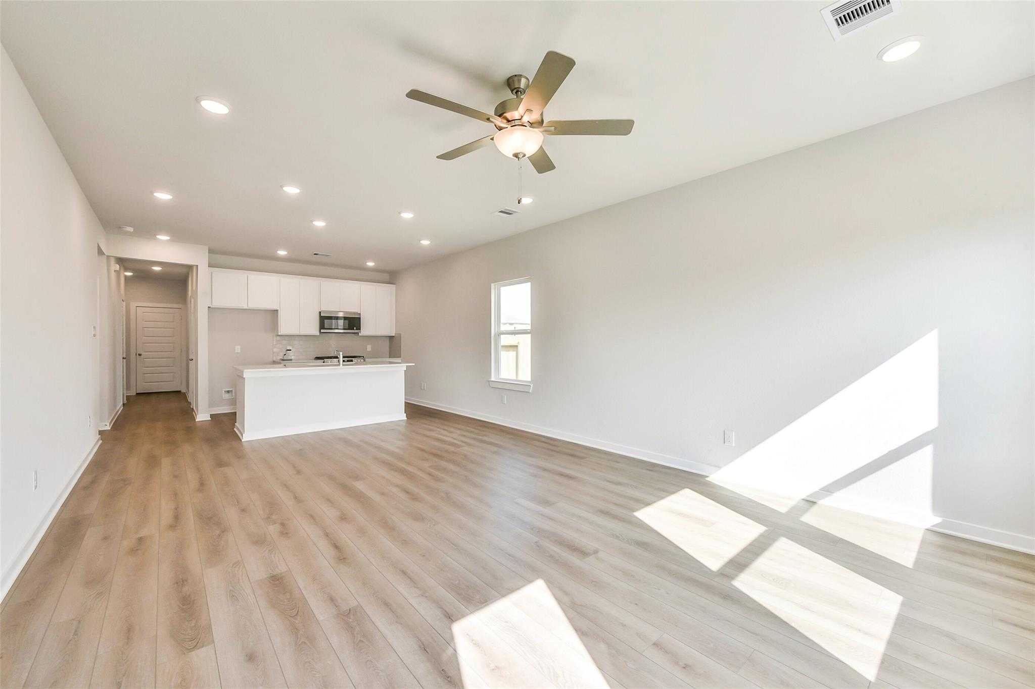 Open-concept living and kitchen area with white cabinets, laminate wood floors, and ceiling fans in Davidson Homes The Comal G, Dayton, Texas