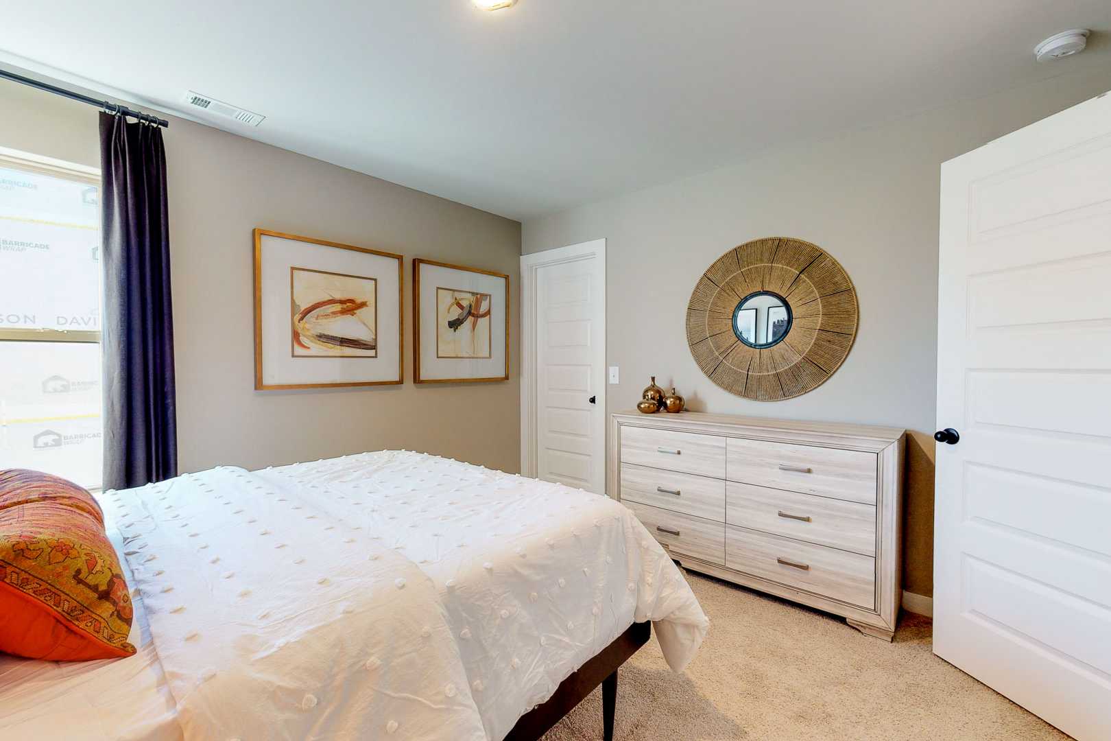 Master bedroom at Liberty Creek in Gallatin TN by Davidson Homes with king bed, white duvet, orange pillows, wooden dresser, round mirror