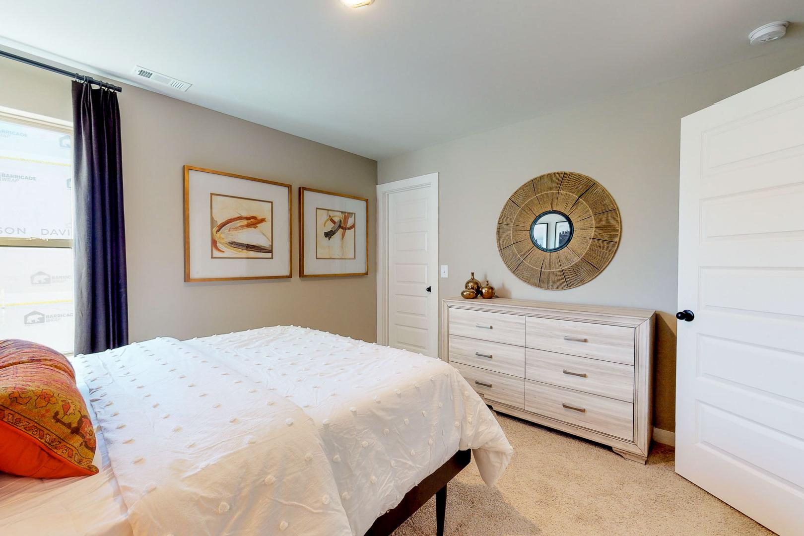 Master bedroom at Liberty Creek in Gallatin TN by Davidson Homes with king bed, white duvet, orange pillows, wooden dresser, round mirror