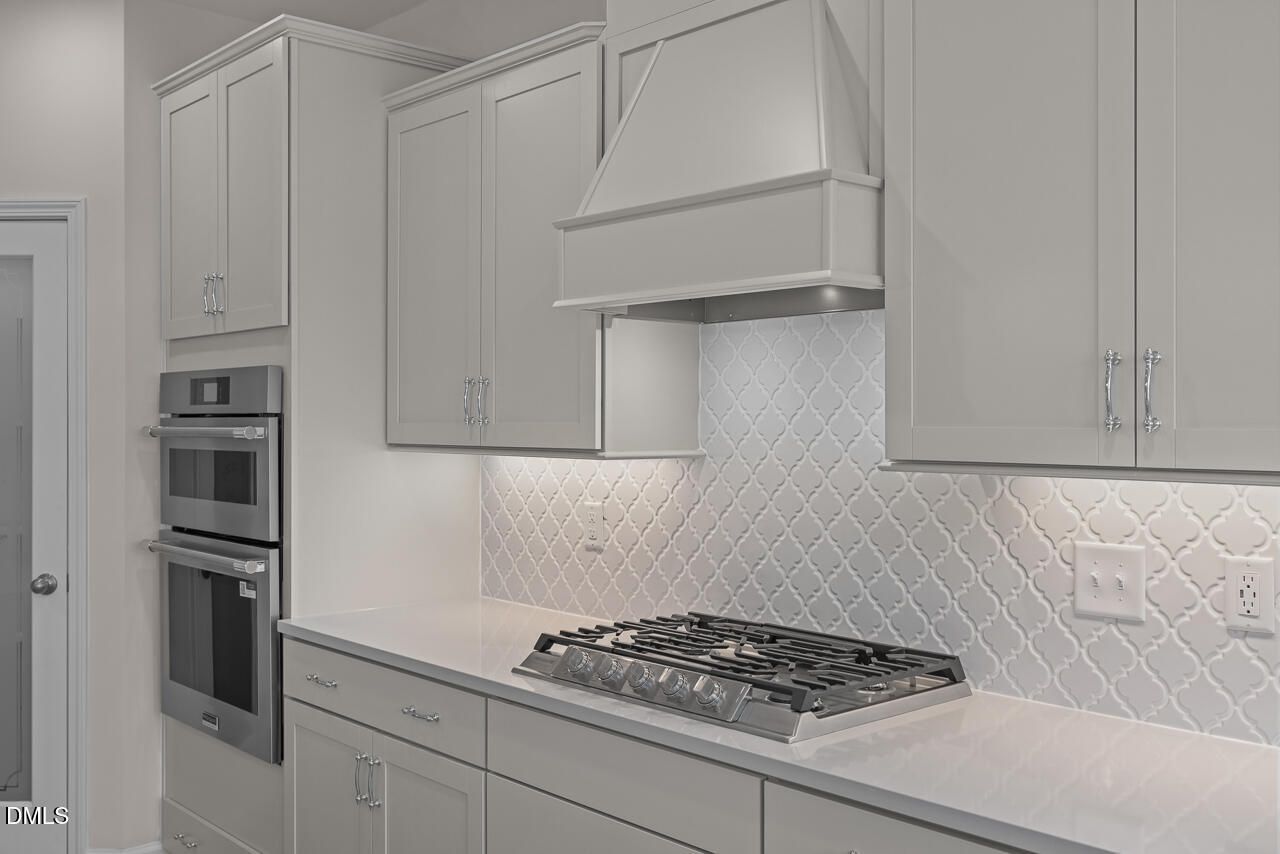 Elegant white shaker kitchen with herringbone subway tile backsplash, double wall oven, gas cooktop in Davidson Homes The Cypress D II, Angier, NC