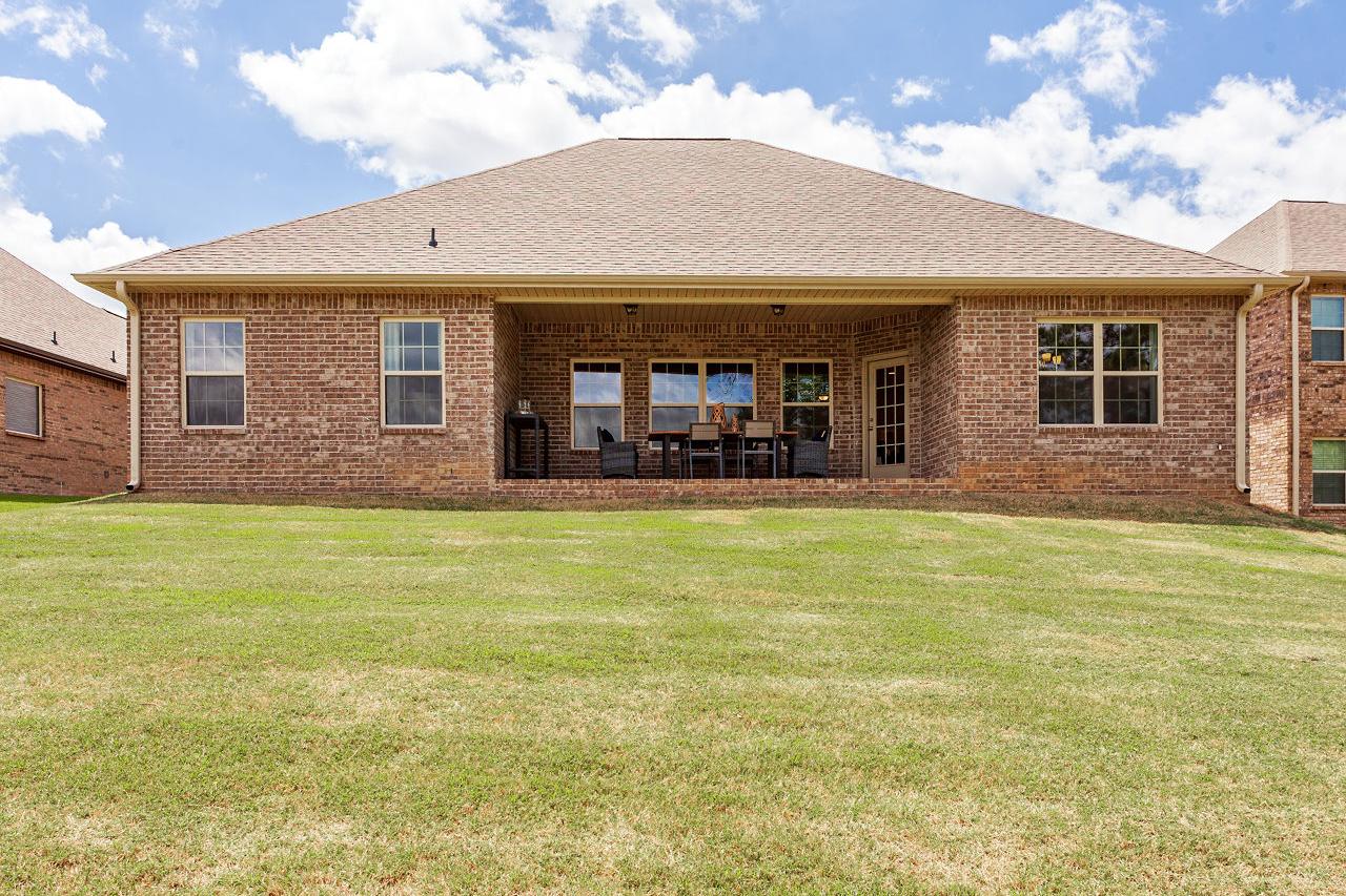 Brick home rear exterior with covered patio, dining set, and lush green lawn at Laurenwood Preserve in Madison, Alabama