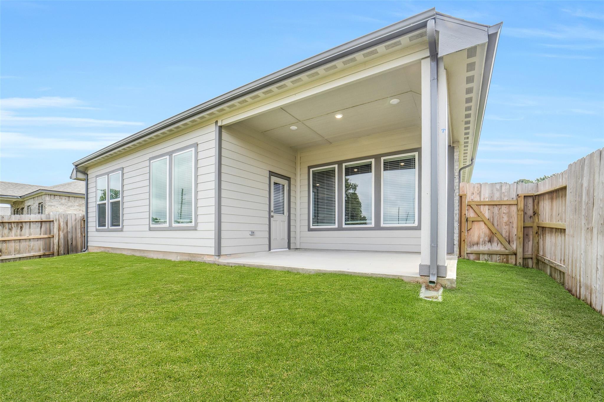 Covered patio with large windows and fenced lush green backyard in Davidson Homes The Acadia C, Magnolia, Texas