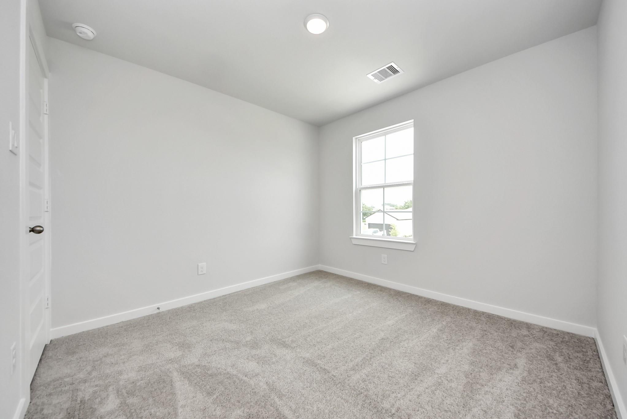 Bright, carpeted bedroom with neutral walls in The Blanco E floor plan at The Villages at WestPointe in Dayton, Texas.