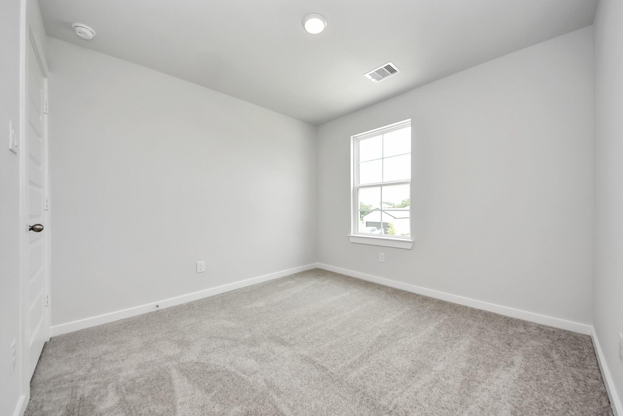 Bright, carpeted bedroom with neutral walls in The Blanco E floor plan at The Villages at WestPointe in Dayton, Texas.