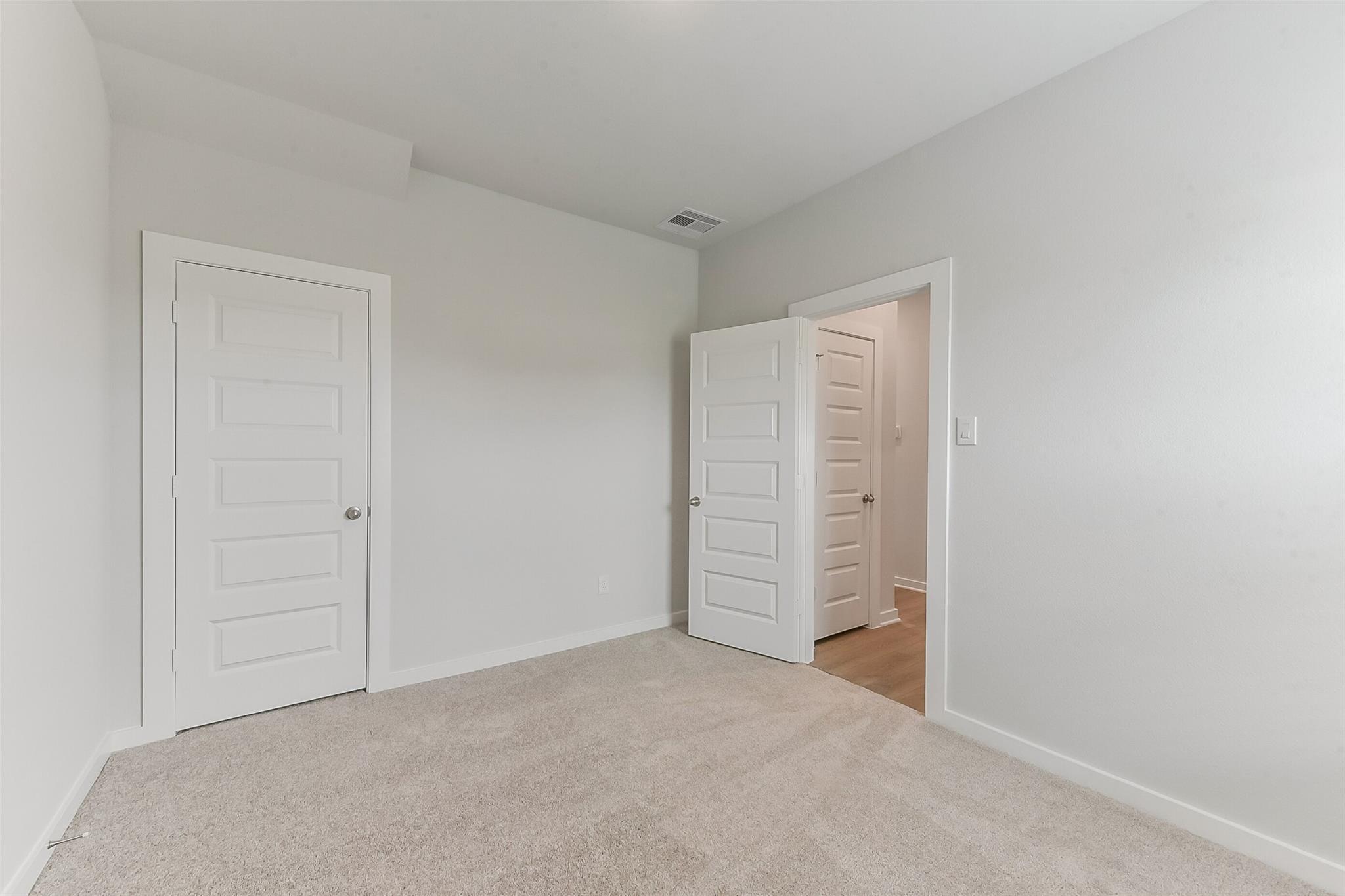 Spacious secondary bedroom featuring neutral gray walls, beige carpet, and double white doors to adjacent bath in Davidson Homes Sabine F, Dayton TX