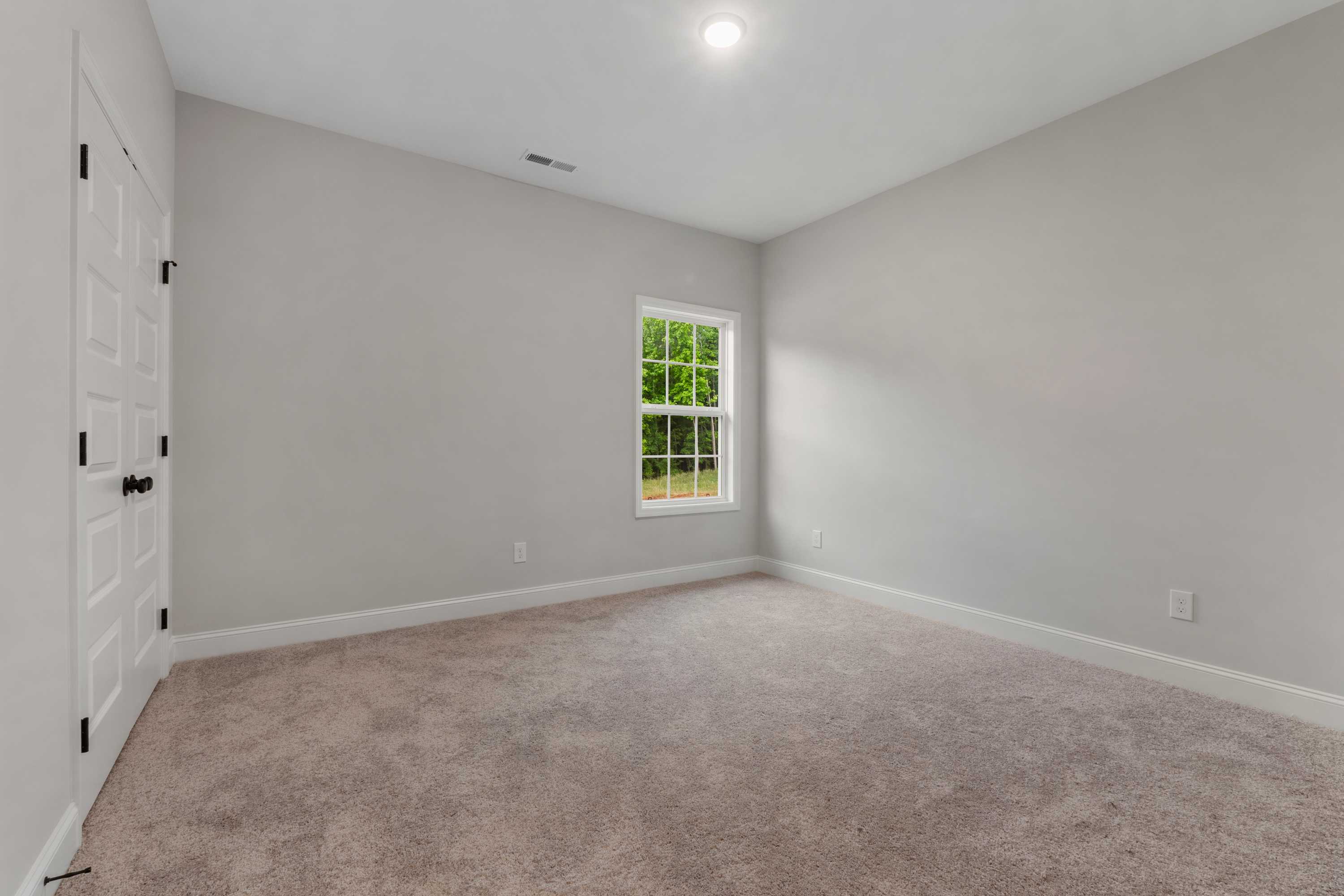 Spacious secondary bedroom in The Oxford home by Davidson Homes with gray walls, large window, carpet flooring, Meridianville AL