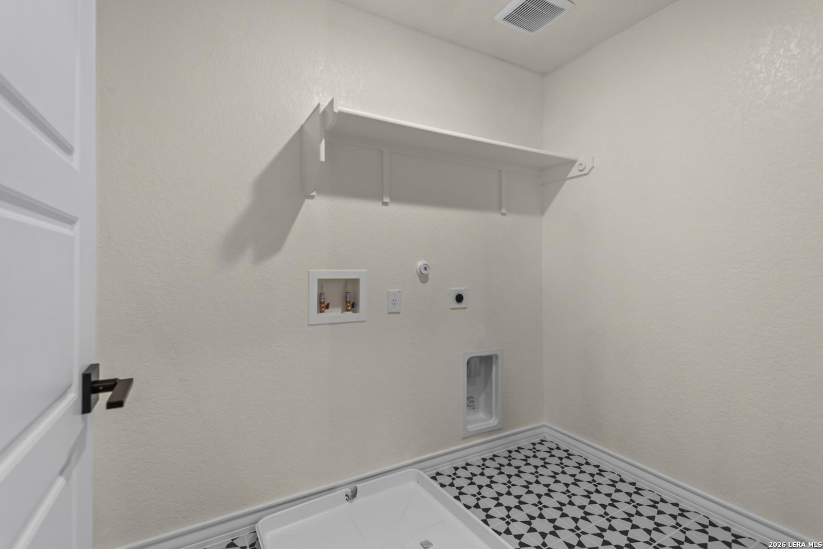 Laundry room with patterned tile floor, washer hookups, and shelving in The Danbury H home in Potranco Oaks, Castroville.