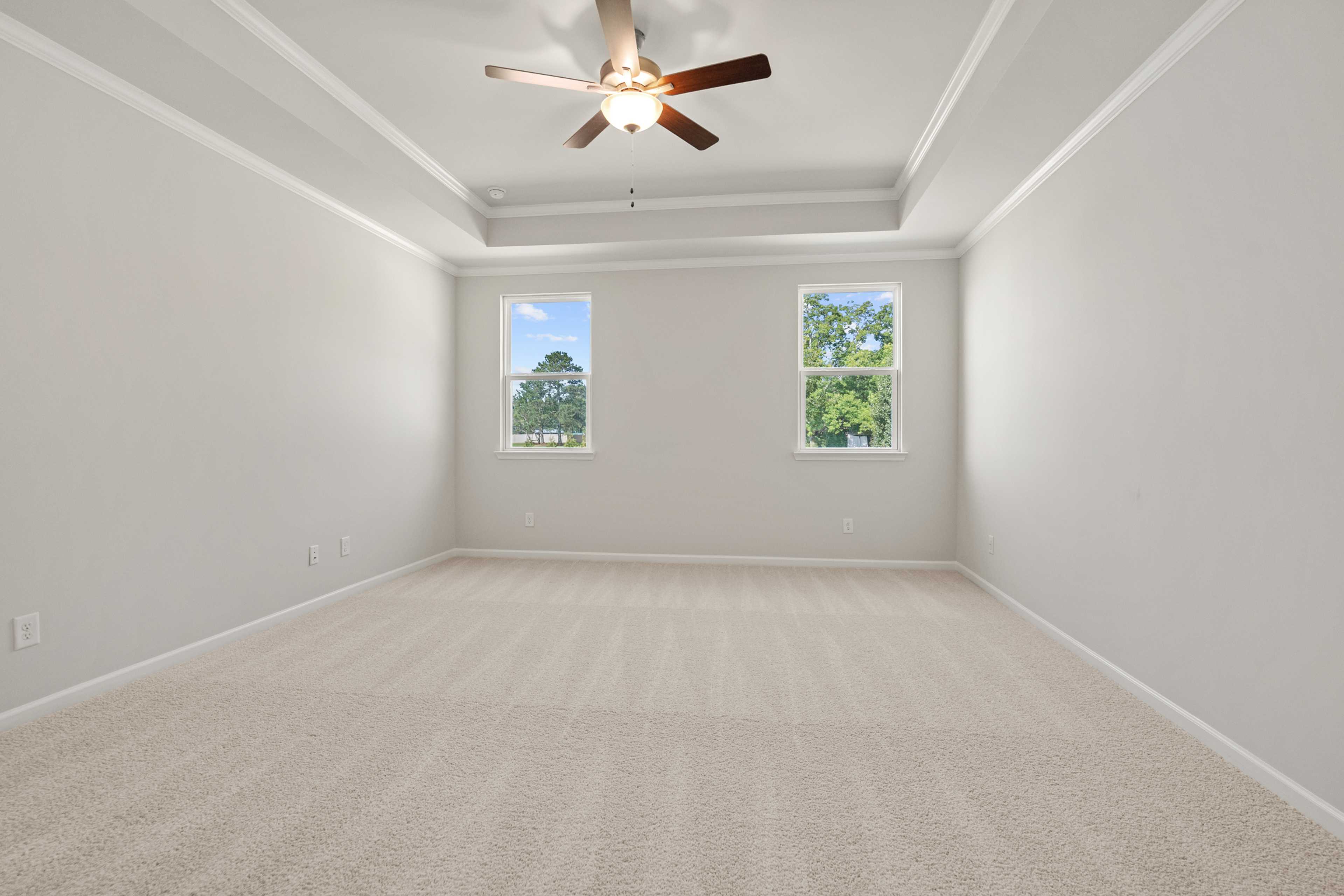 Spacious bedroom at Everleigh in Locust Grove GA by Davidson Homes with ceiling fan, neutral walls, carpet floors and large windows