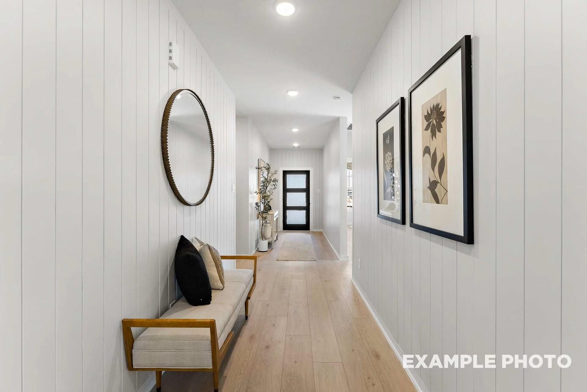 Elegant hallway with white shiplap walls, oak hardwood floors, round gold mirror, upholstered bench and art in The Everett C 4-bedroom home, Dayton, Texas