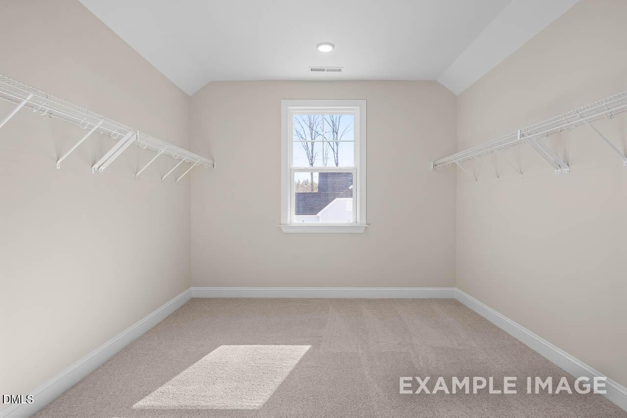 Spacious walk-in closet with beige walls, wooden shelving, and window in Davidson Homes The Crawford D, Angier, North Carolina