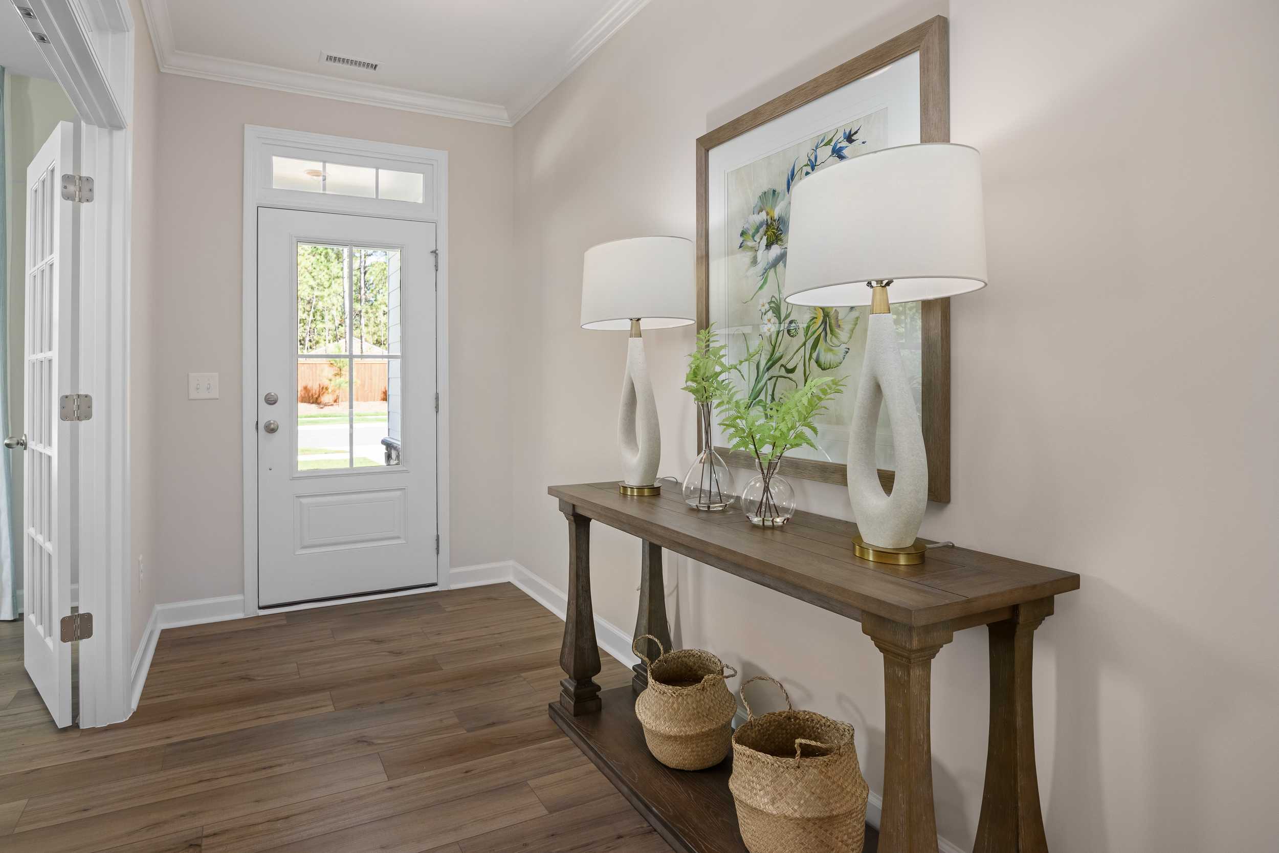 Spacious entryway of The Hickory II E by Davidson Homes with wooden console table, white lamps, abstract artwork, and hardwood floors in Holly Springs