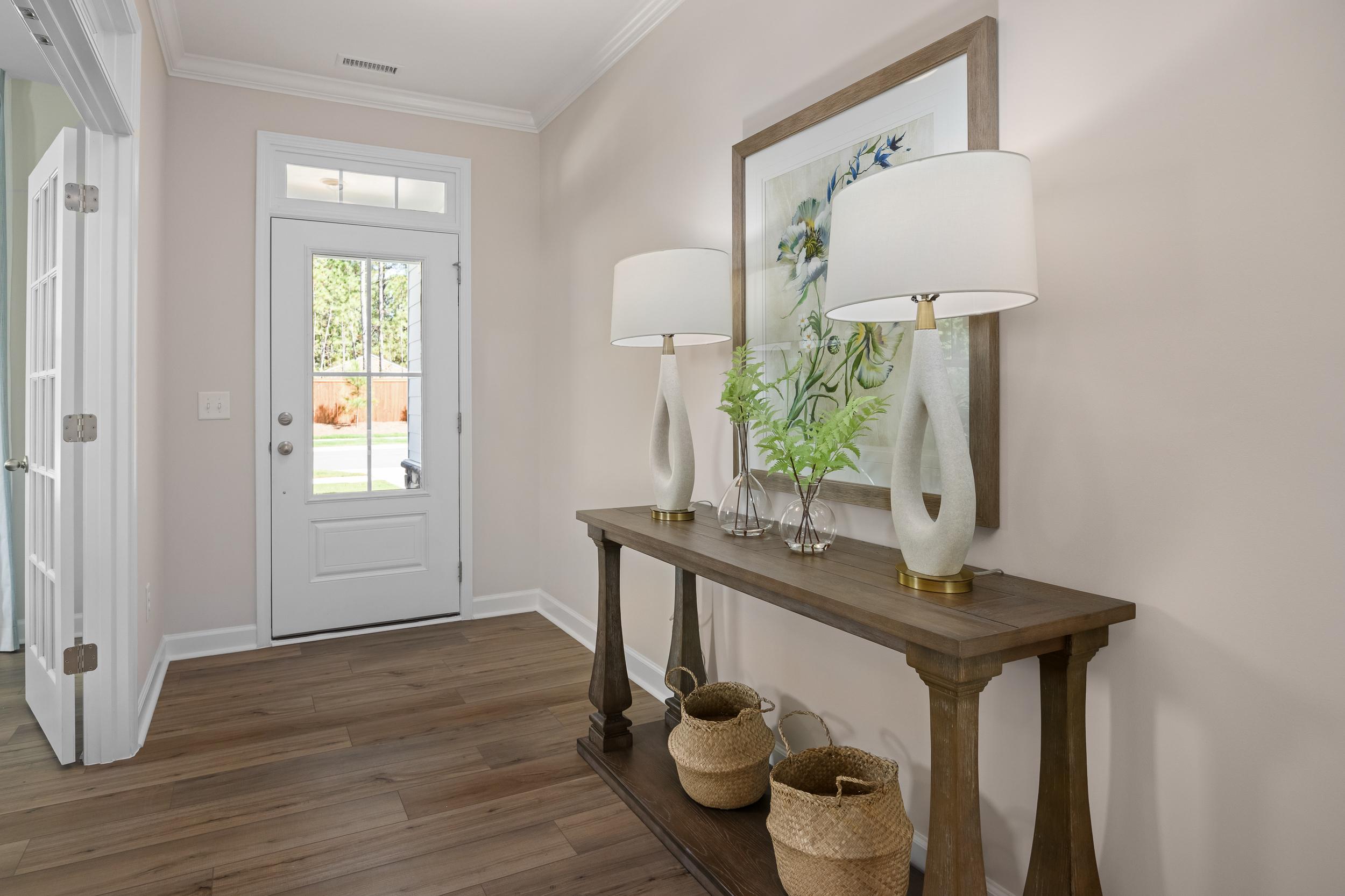 Spacious entryway in The Hickory II home with console table, lamps, vase, and artwork on hardwood floors