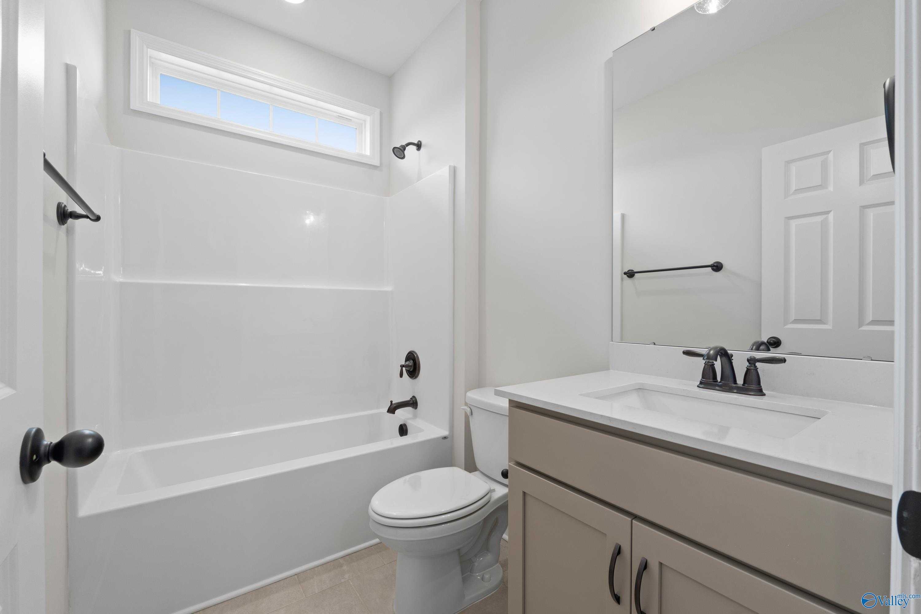 Modern guest bathroom featuring white subway tile tub-shower combo, beige vanity, and large mirror in Davidson Homes The Kirkland, Creekside, Harvest, AL