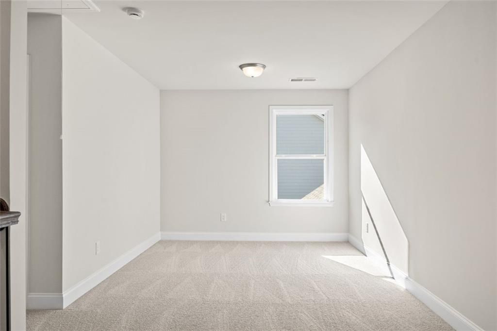 Bright empty bedroom with light gray walls, beige carpet, and large window in Davidson Homes The Ash C at Wehunt Meadows, Hoschton