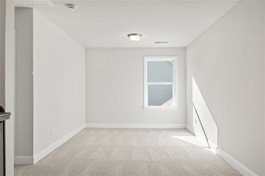 Bright empty bedroom with light gray walls, beige carpet, and large window in Davidson Homes The Ash C at Wehunt Meadows, Hoschton