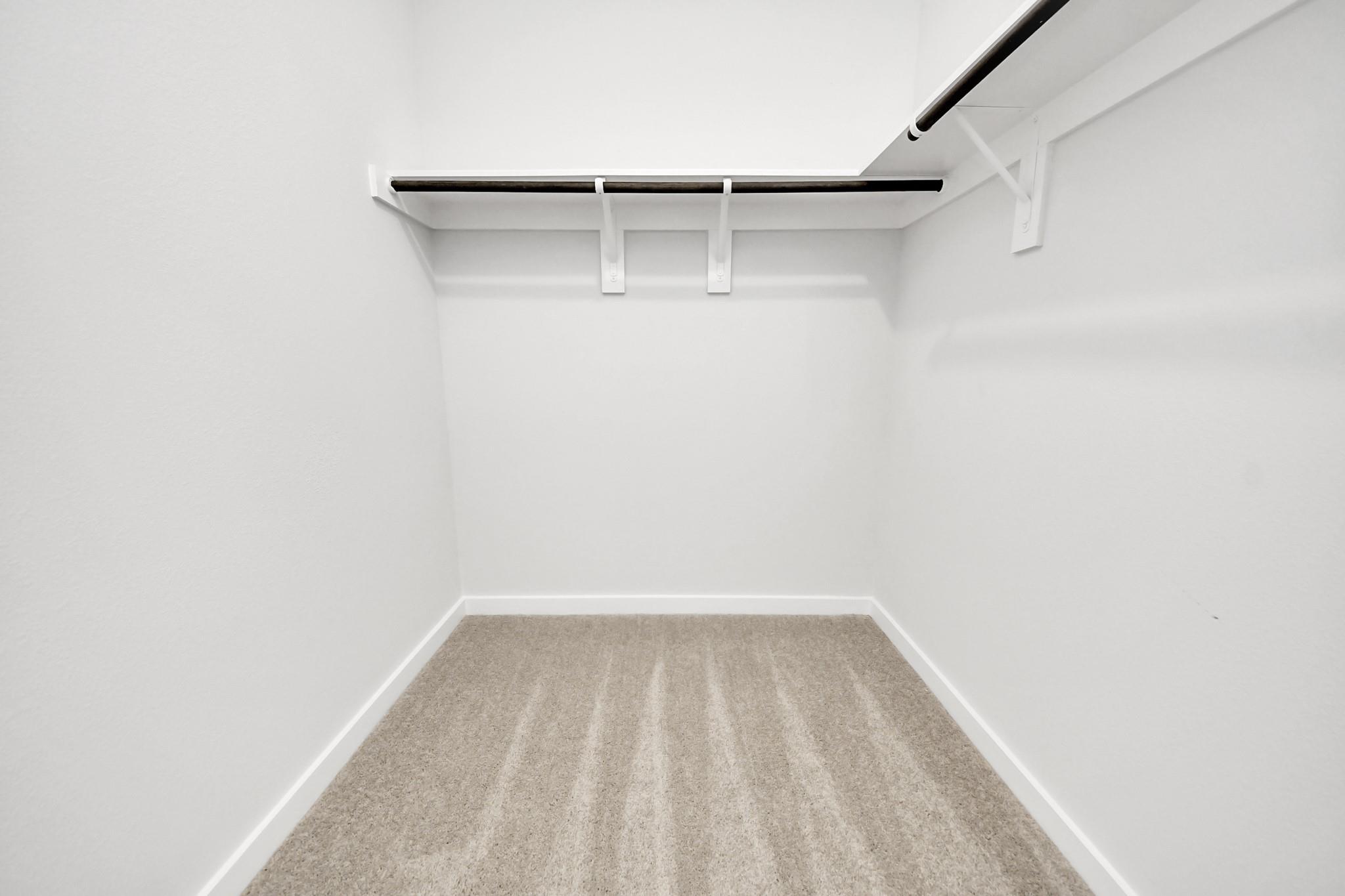 Spacious walk-in closet with hanging rods, white walls, and carpet flooring in Davidson Homes The Costa A, Emberly, Beasley, Texas