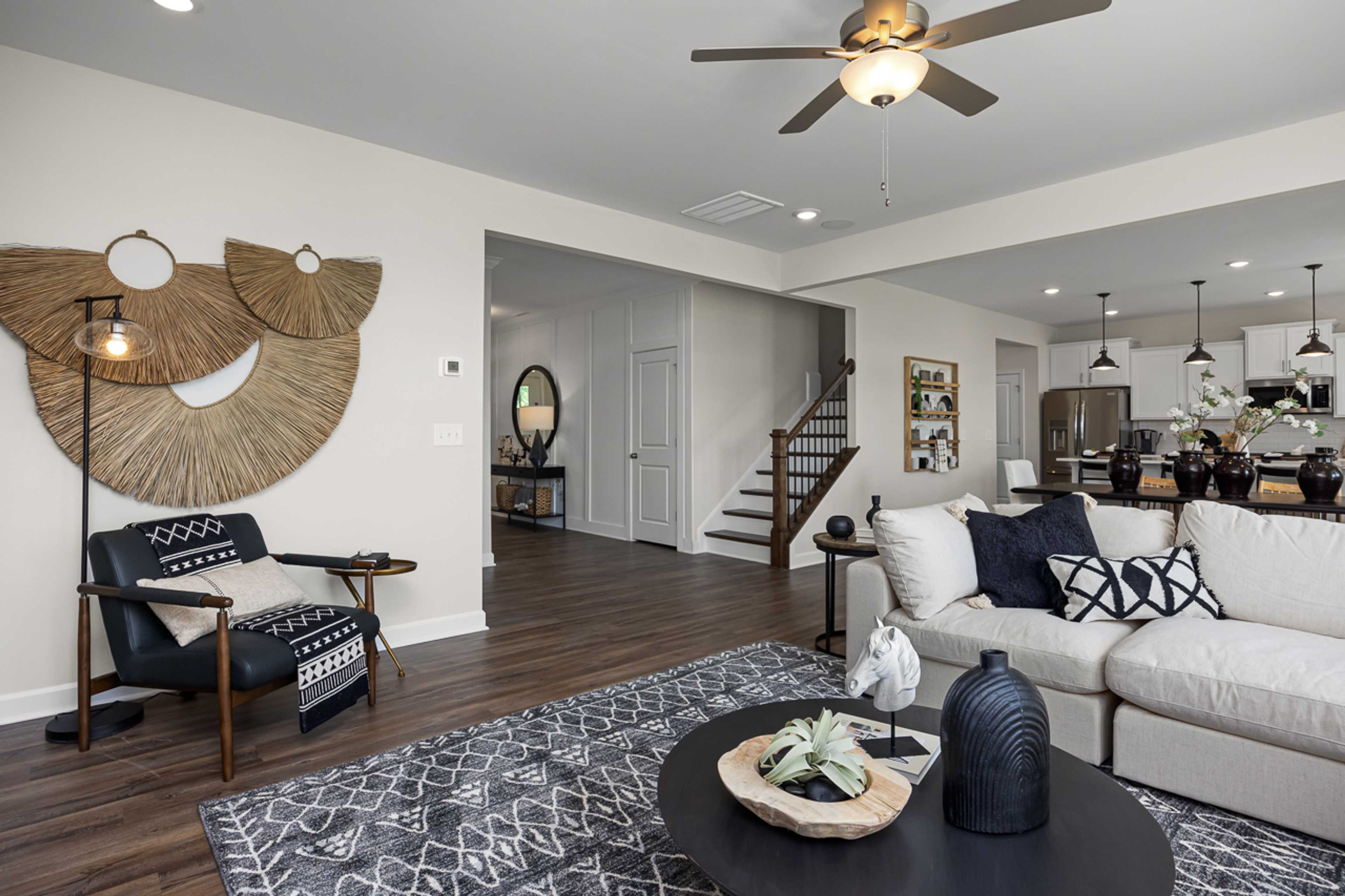 Open-concept living room at Wellers Knoll in Lillington NC with hardwood floors, white sofa, woven wall art and adjacent kitchen