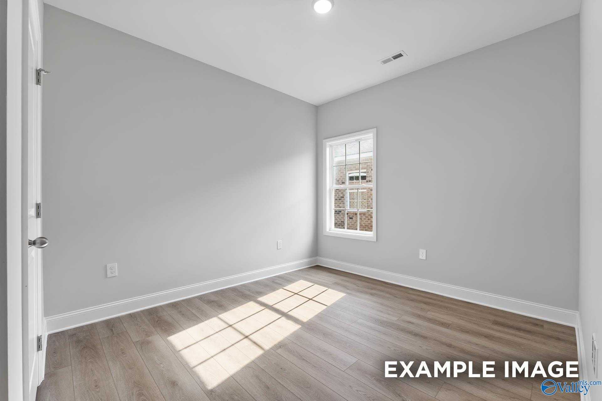 Bright bedroom with gray walls, large window streaming sunlight onto luxury vinyl plank floors in Davidson Homes The Asheville C, Huntsville AL