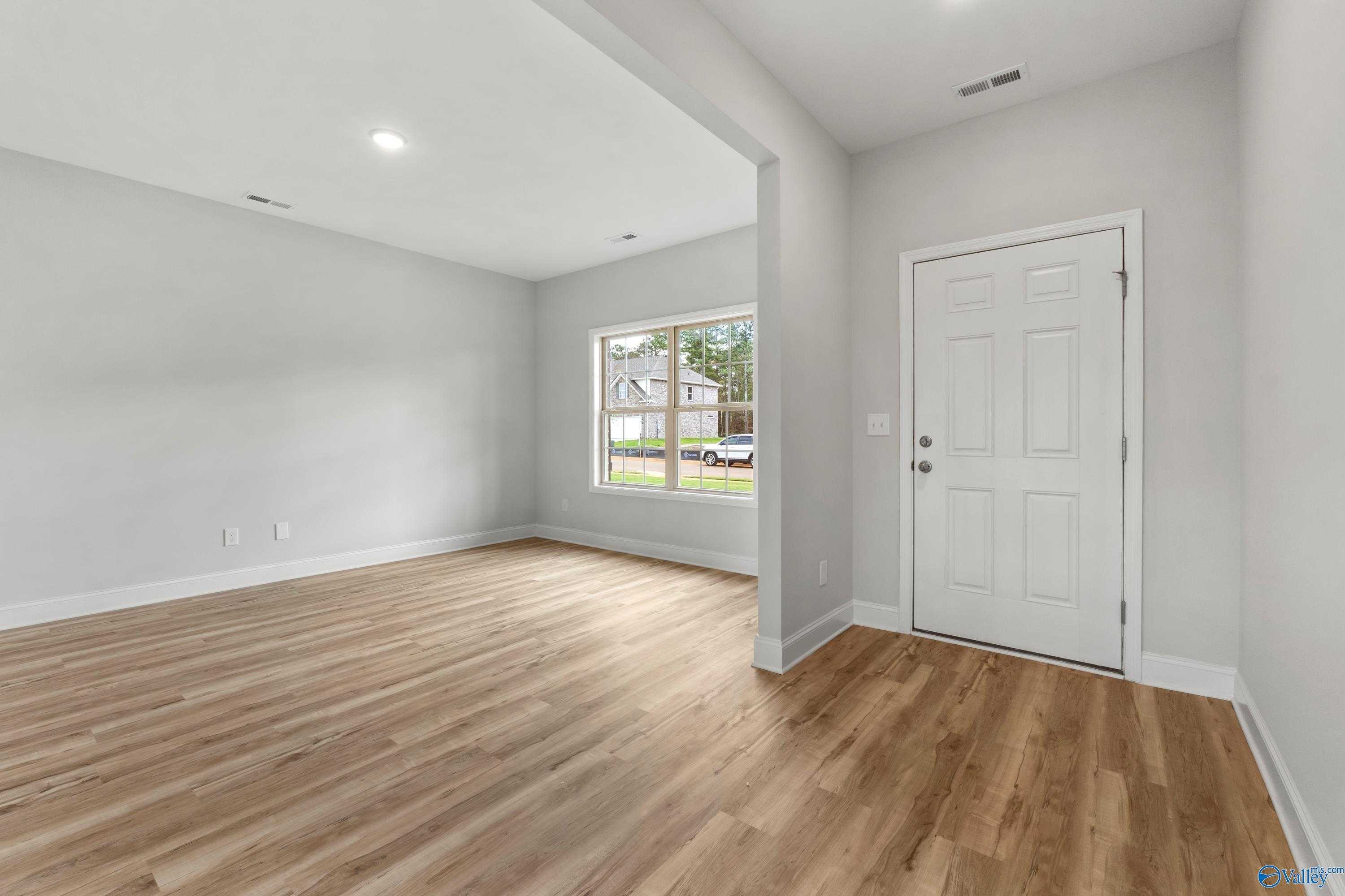 Empty secondary bedroom with light oak hardwood floors, large window overlooking yard, and gray walls in Davidson Homes The Chelsea C, Harvest AL