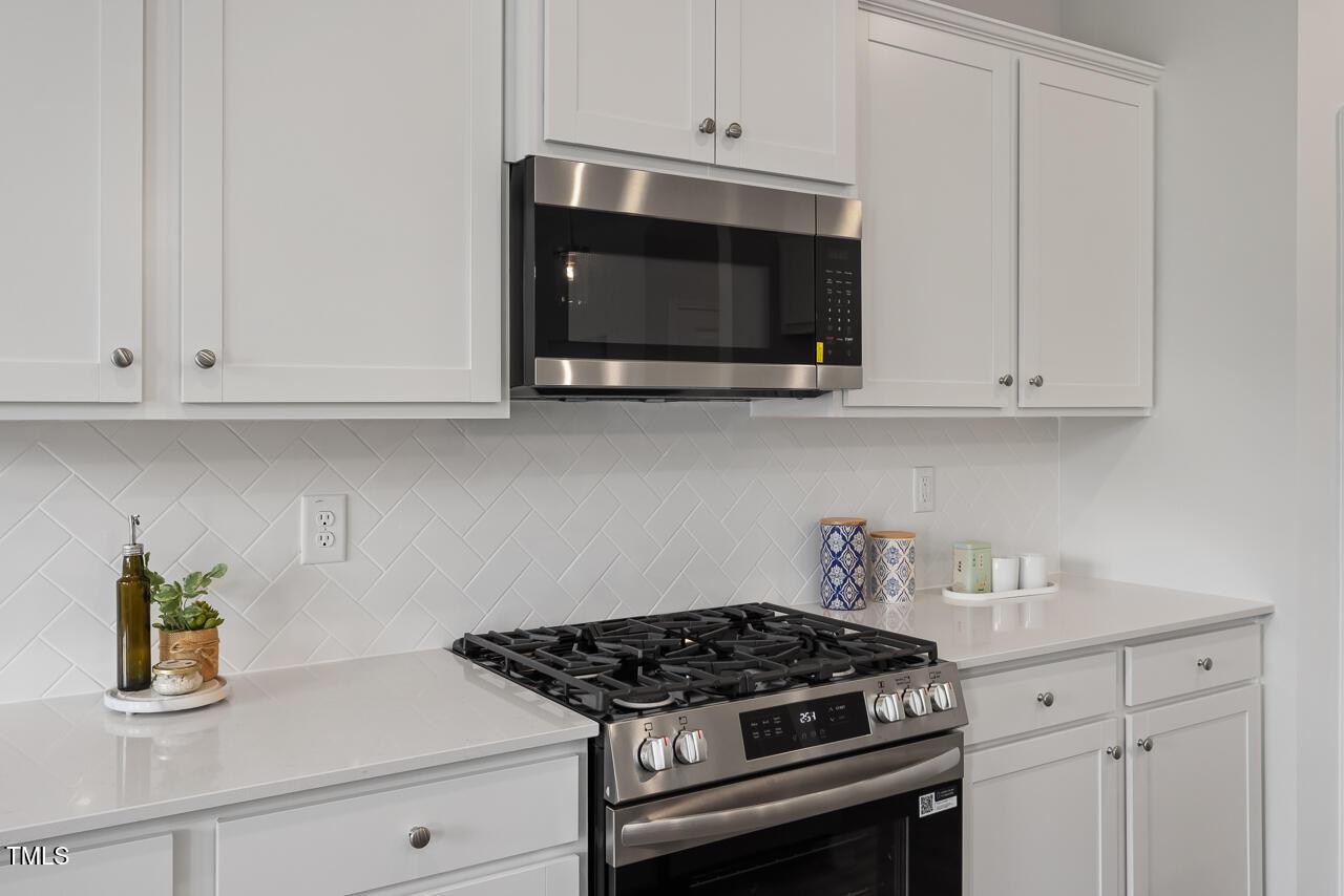Modern white kitchen with stainless steel gas range, microwave, subway tile backsplash in Davidson Homes The Warren, Fuquay-Varina, NC
