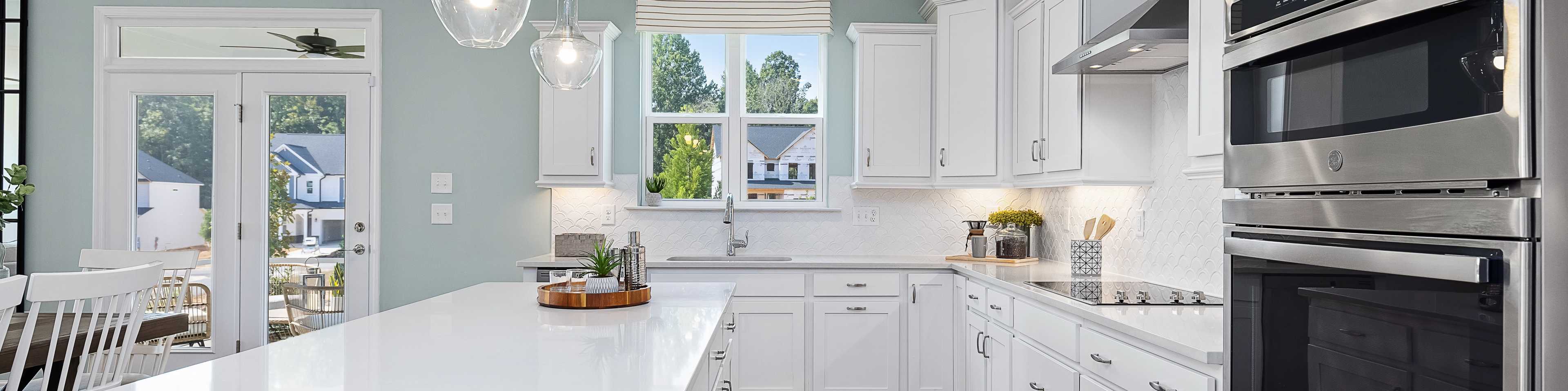 Spacious white shaker kitchen at Addison West in Holly Springs NC with quartz island, hardwood floors, and French doors
