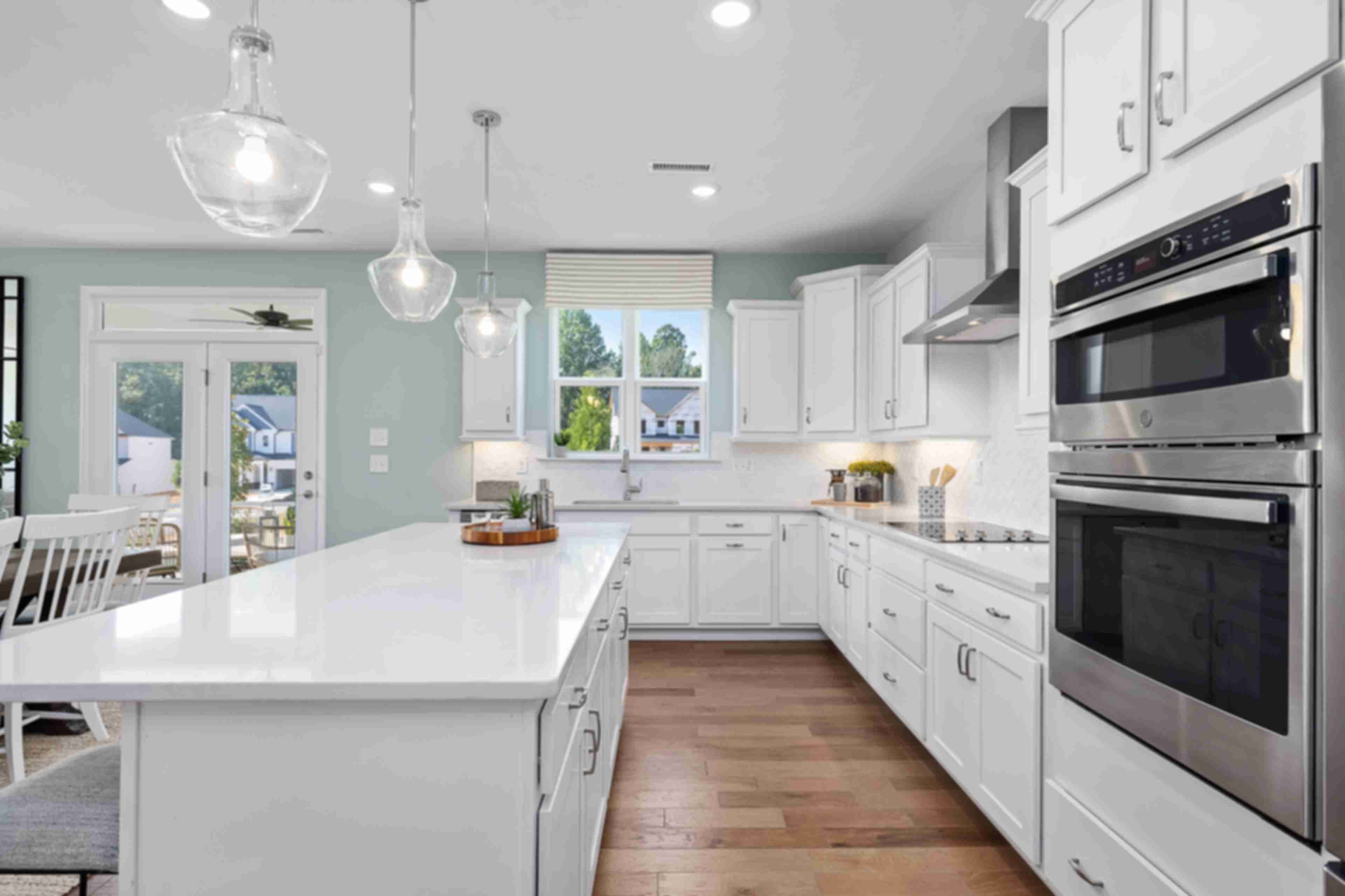 Spacious white shaker kitchen at Addison West in Holly Springs NC with quartz island, hardwood floors, and French doors
