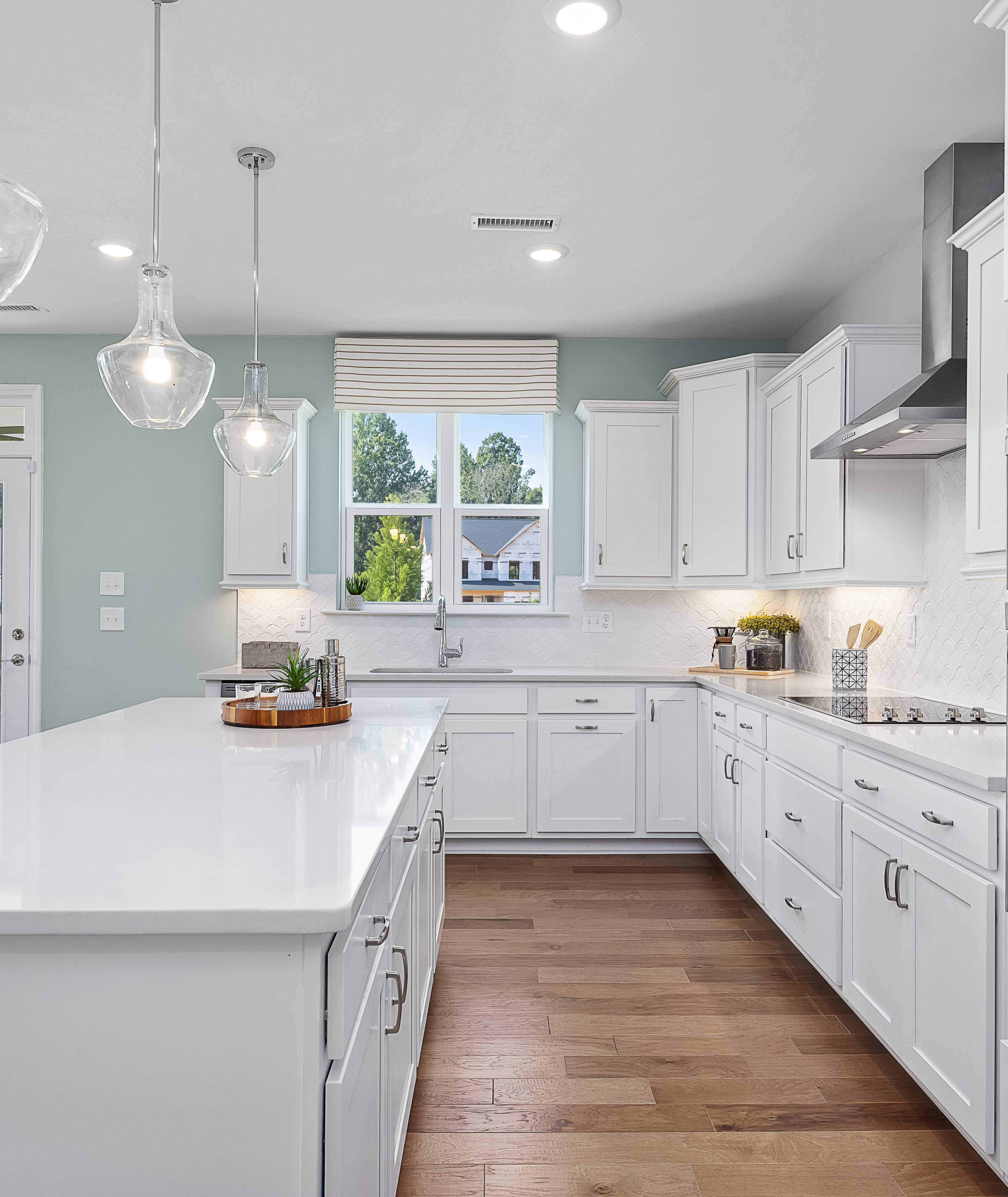 Spacious white shaker kitchen at Addison West in Holly Springs NC with quartz island, hardwood floors, and French doors