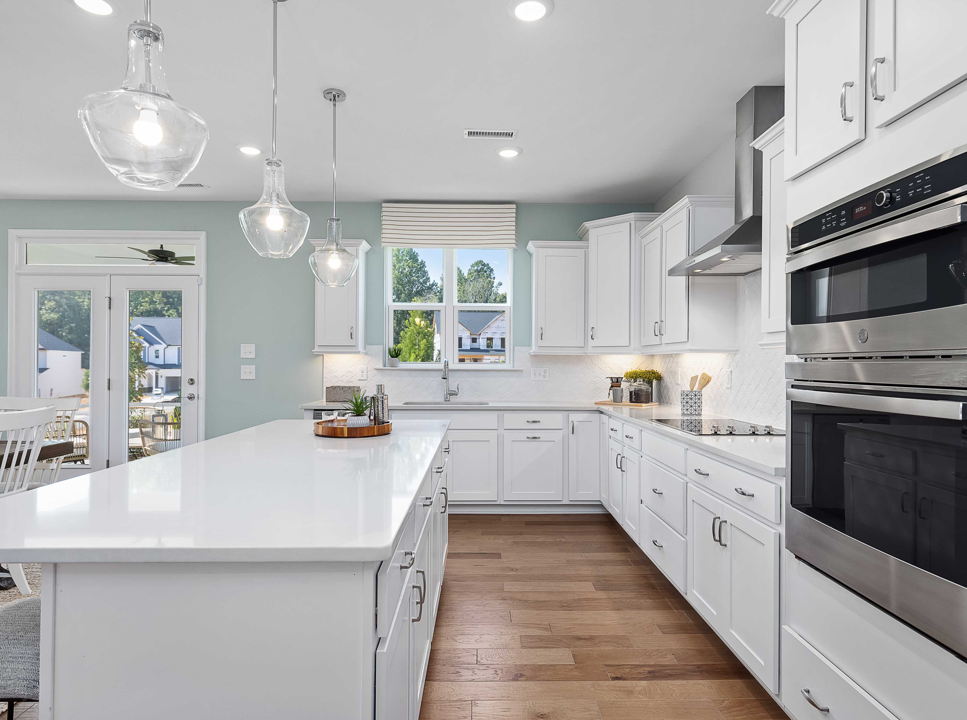 Spacious white shaker kitchen at Addison West in Holly Springs NC with quartz island, hardwood floors, and French doors