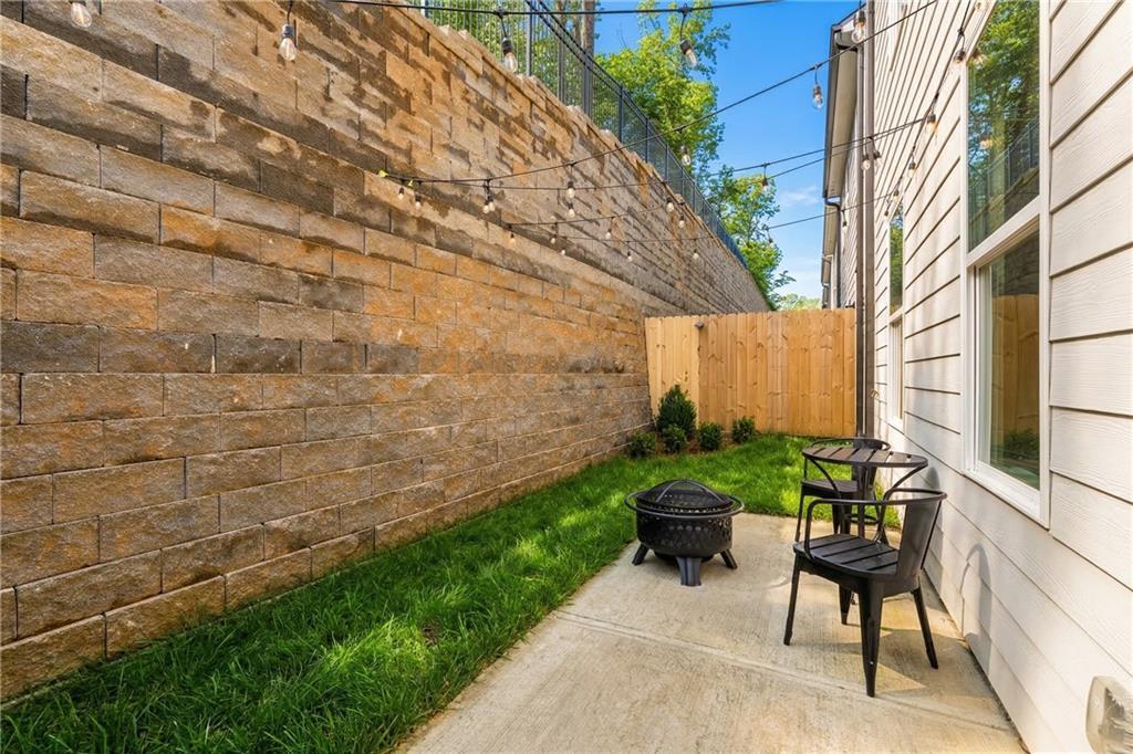 Cozy side yard with stone retaining wall, fire pit, black chairs, and lush grass beside The Marion B home in Kennesaw, Georgia