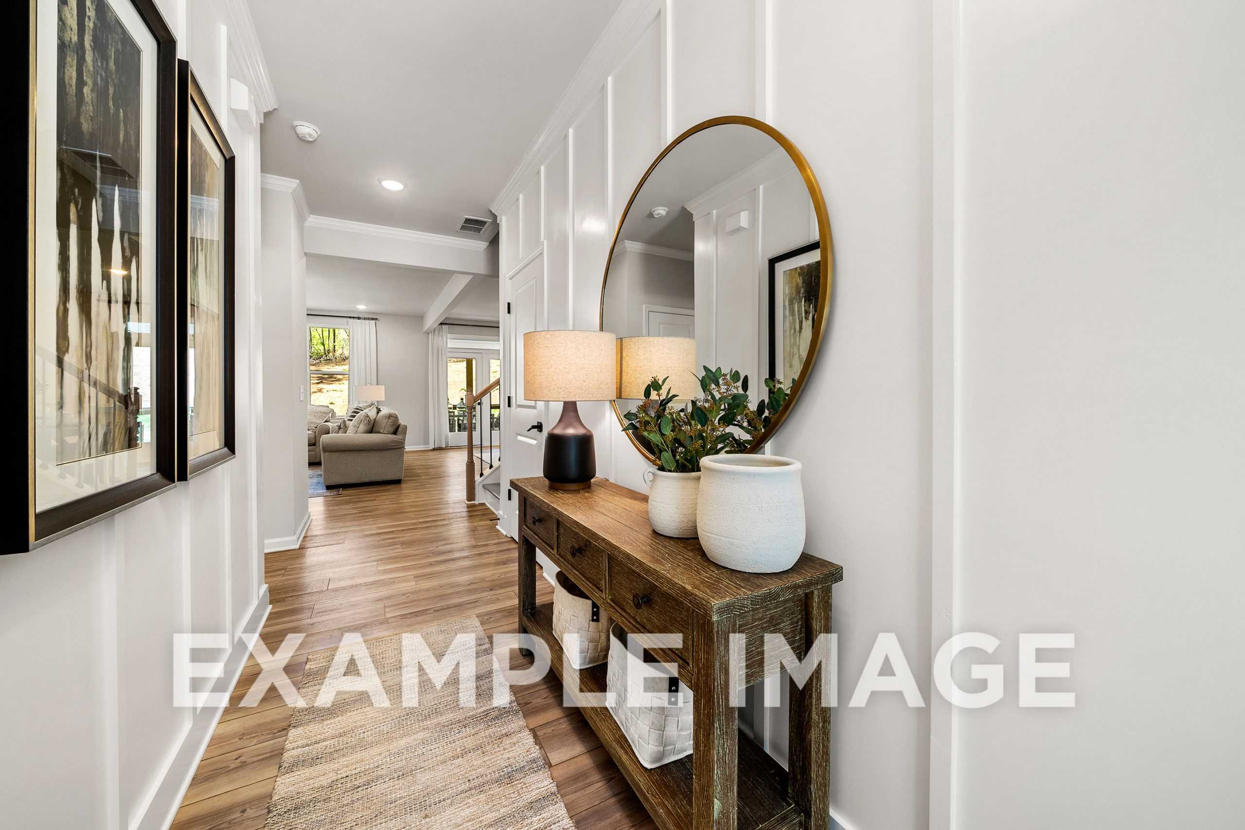 Spacious hallway in The Hickory home with white wainscoting, round gold mirror, wooden console table, lamps, plants, and artwork