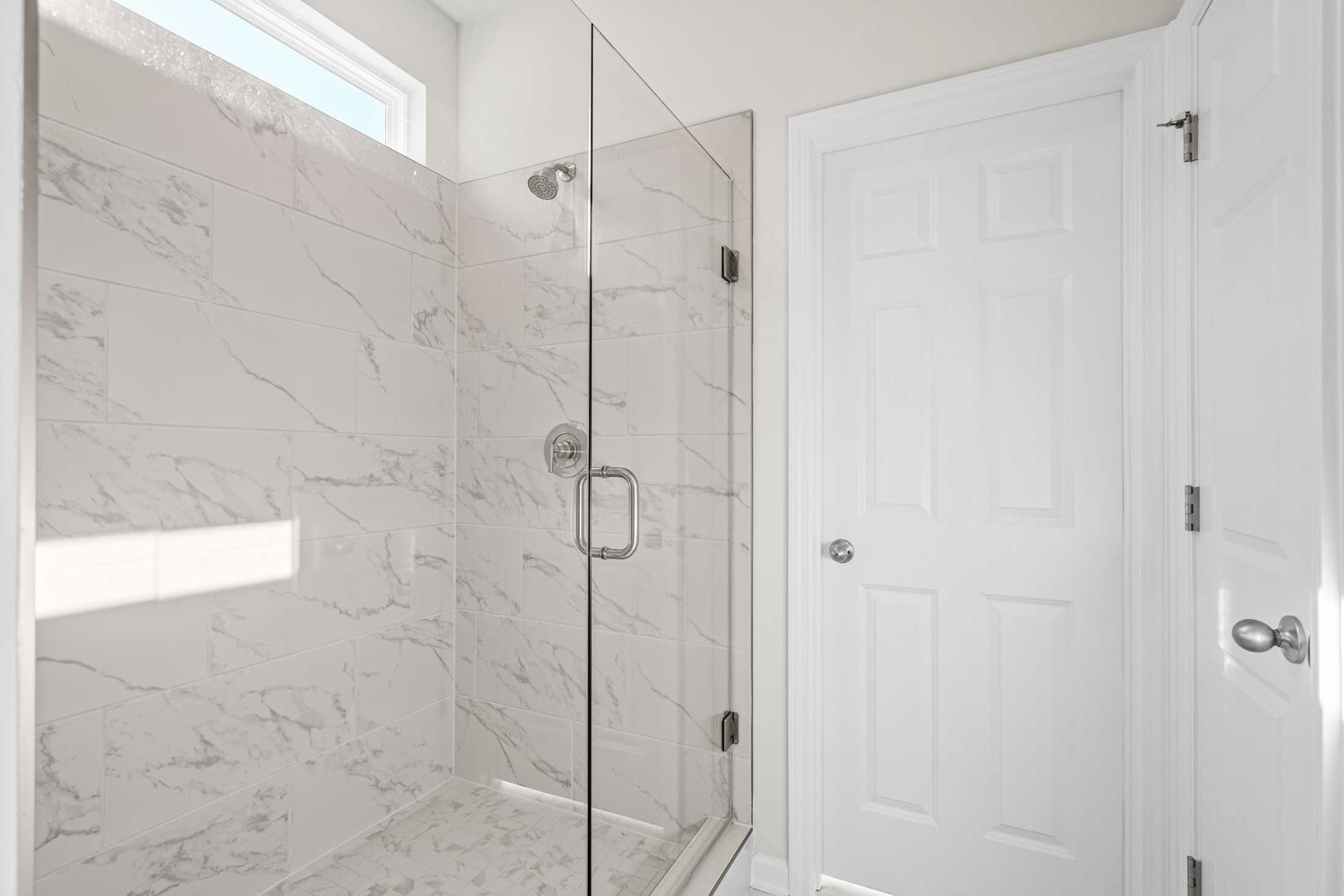 Spacious master suite shower in The Glenwood A with frameless glass enclosure, white marble tiles, and chrome fixtures