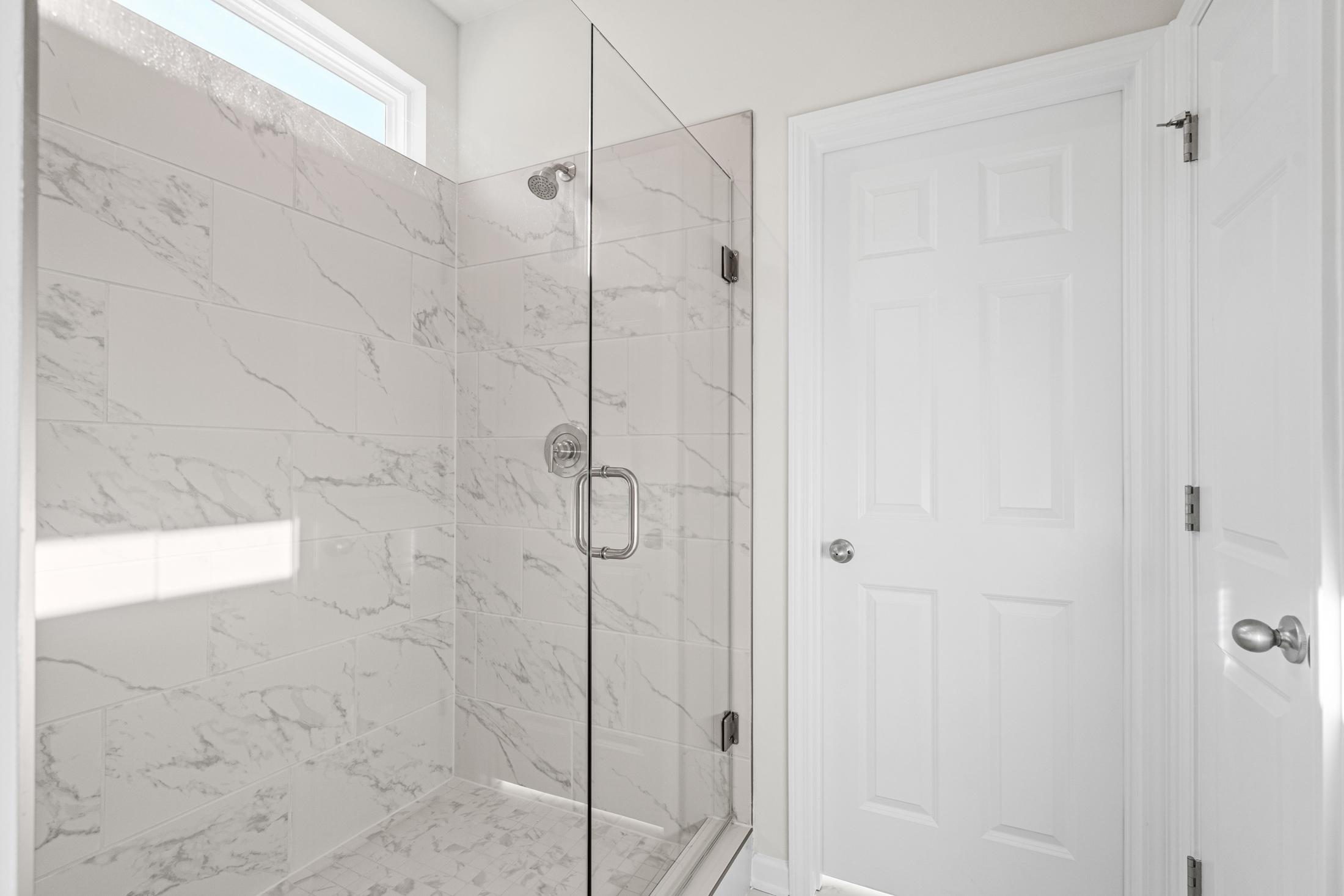 Spacious master suite shower in The Glenwood A with frameless glass enclosure, white marble tiles, and chrome fixtures