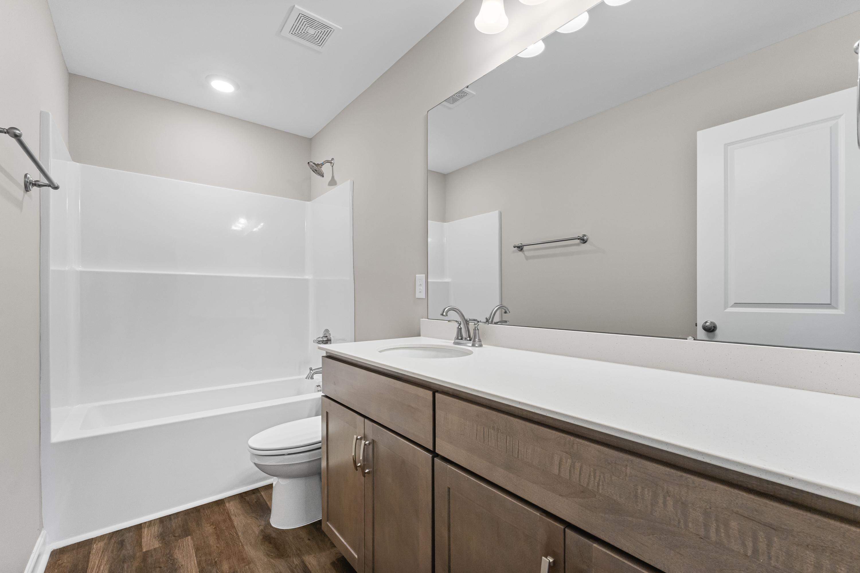 Spacious bathroom in The Haven E by Evermore Homes featuring white tub-shower combo, brown wood vanity, and neutral walls