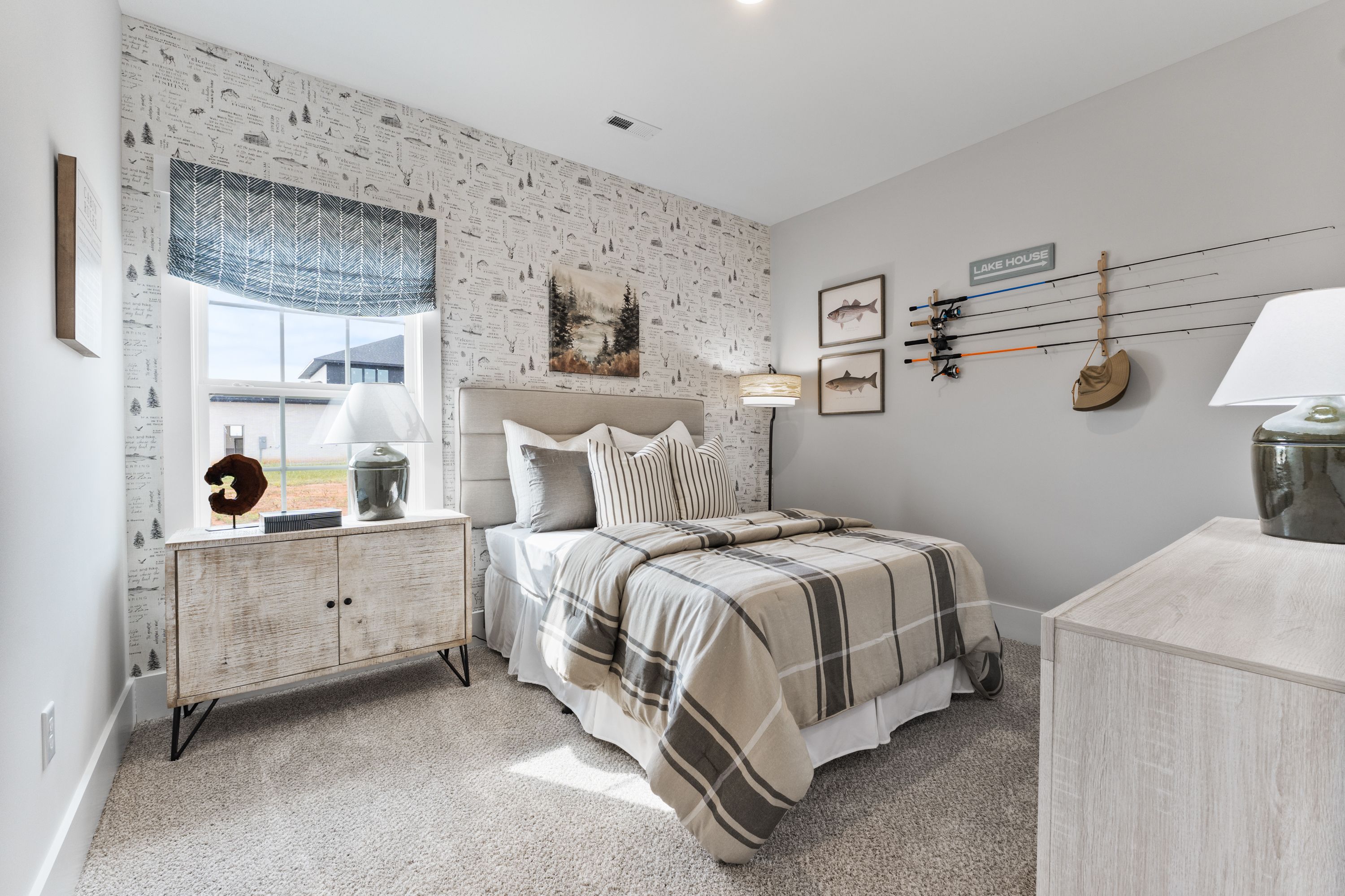 Cozy bedroom at River Road Estates in Decatur Alabama with adventure-themed wallpaper, plaid bedding, and fishing rod rack