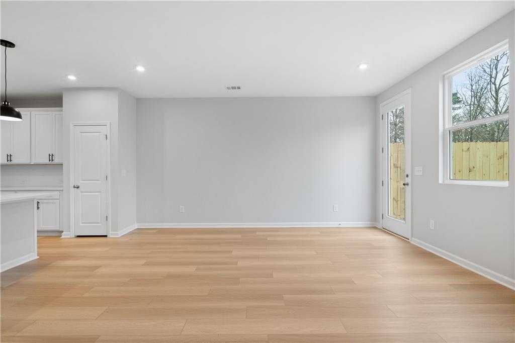 Open-concept living room with hardwood floors, white kitchen cabinets, and sliding glass door to fenced backyard in Davidson Homes The Durant A, Emerson, Georgia