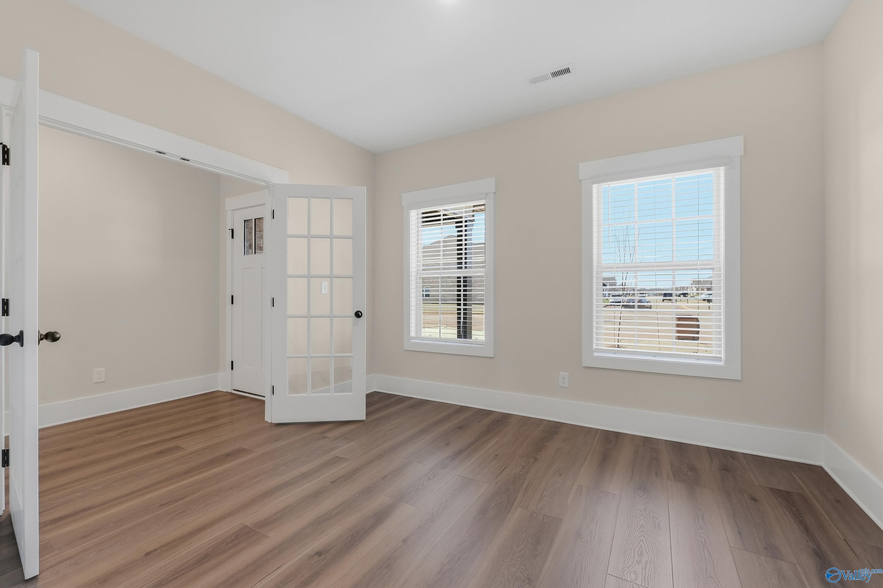 Bright bedroom with beige walls, luxury vinyl plank floors, open French doors, and sunny windows in Davidson Homes The Shelby A, Athens, Alabama